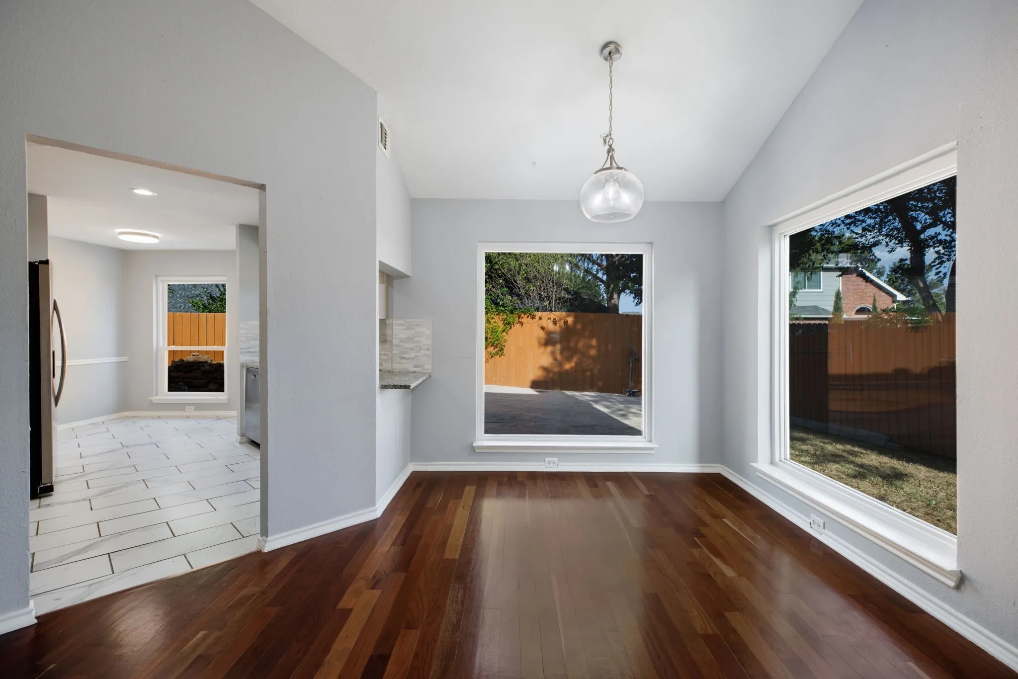 Hardwood-finish flooring, vaulted ceiling, contemporary pendant light fixture, large windows, and a pass-through counter with a tiled backsplash