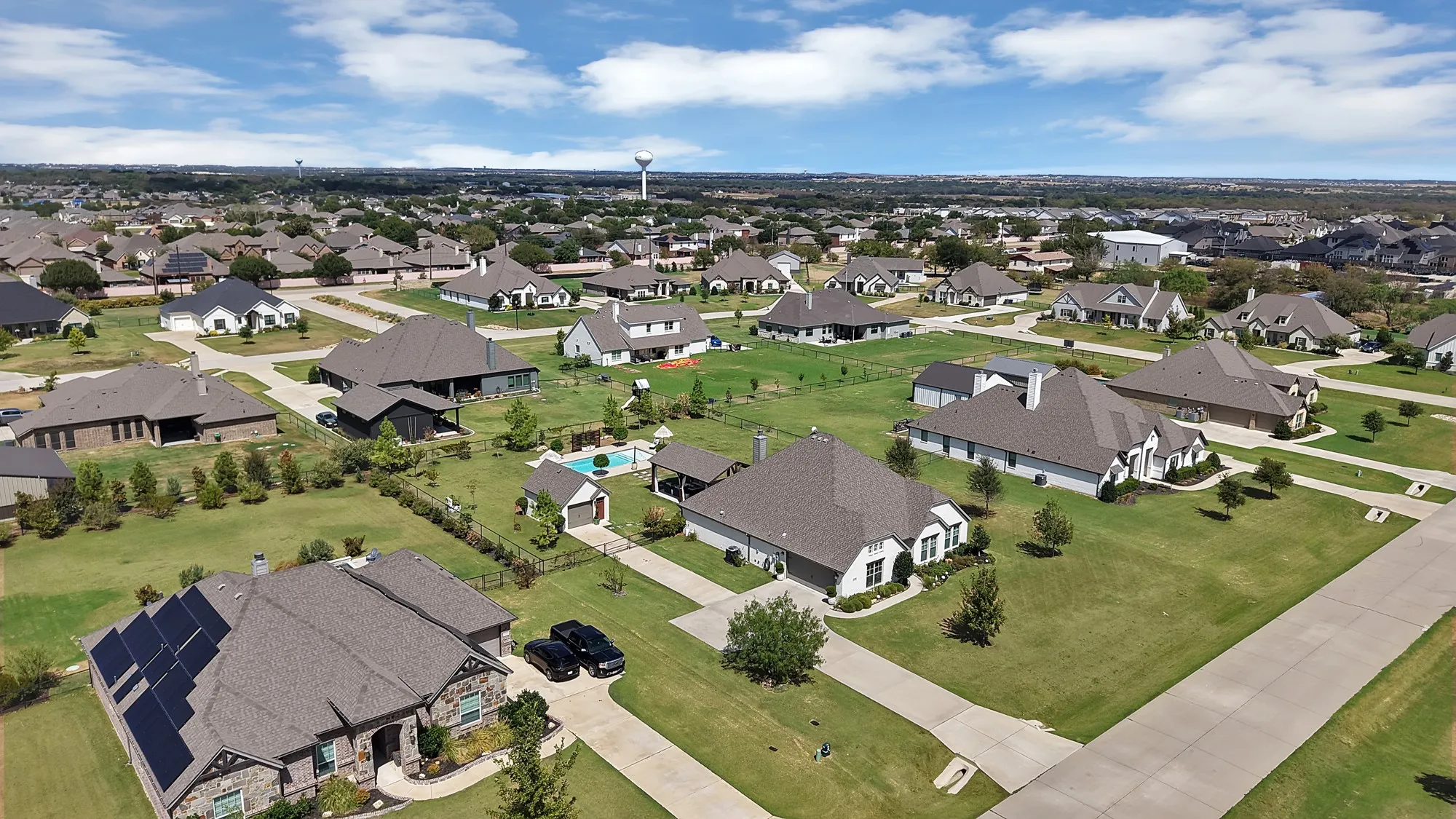 Expansive neighborhood with diverse architectural styles, visible solar panels on one residence, large lots, and a water tower in the distance