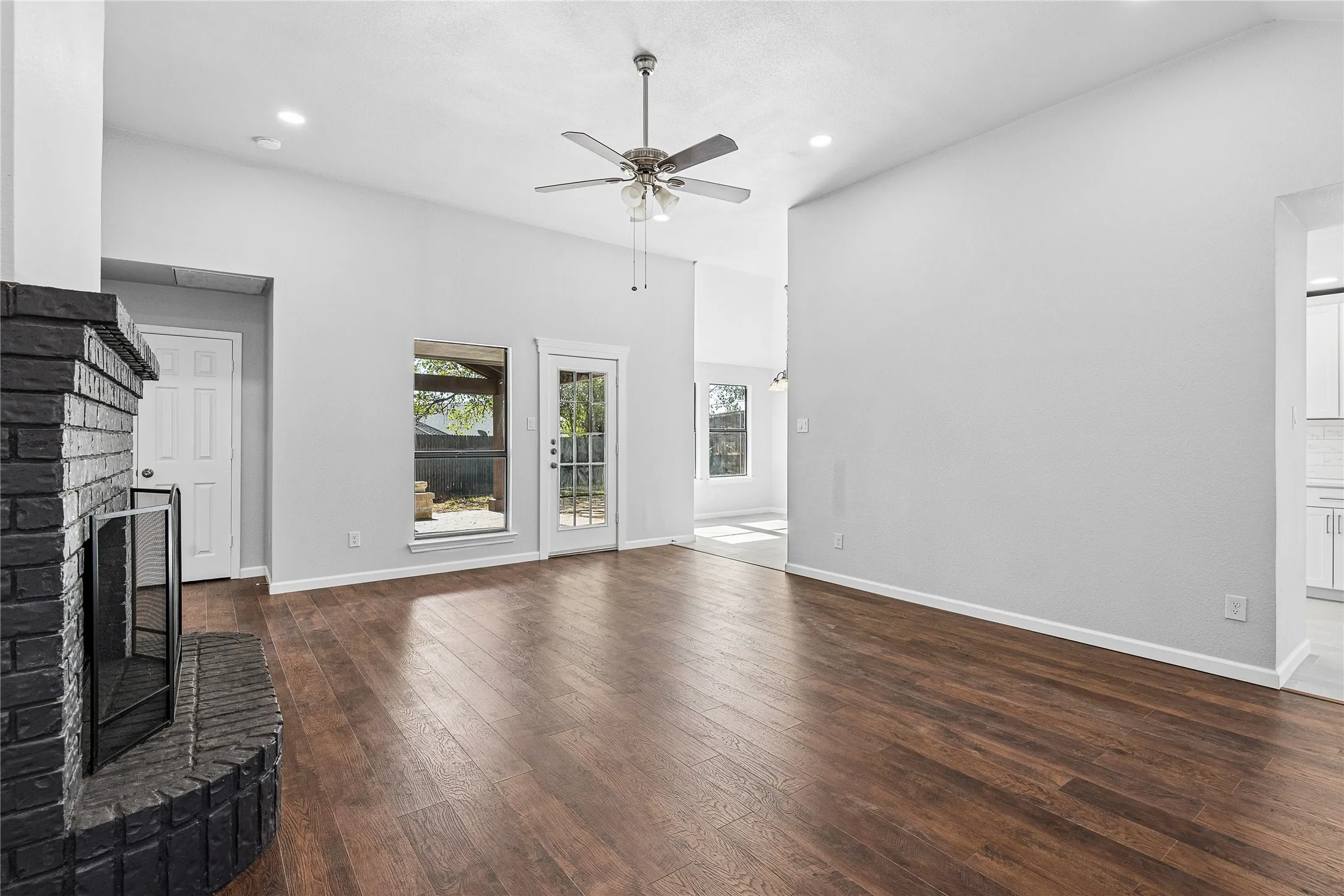 Vaulted ceilings, wood-finish flooring, recessed lighting, and a dark brick fireplace with a hearth