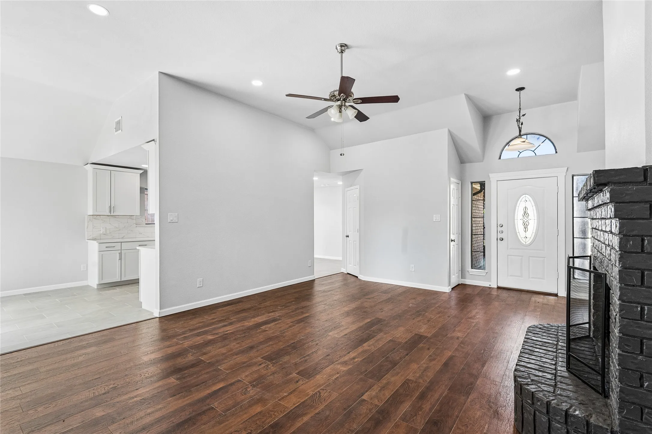Wood-finish flooring, vaulted ceilings, recessed lighting, and a black brick fireplace