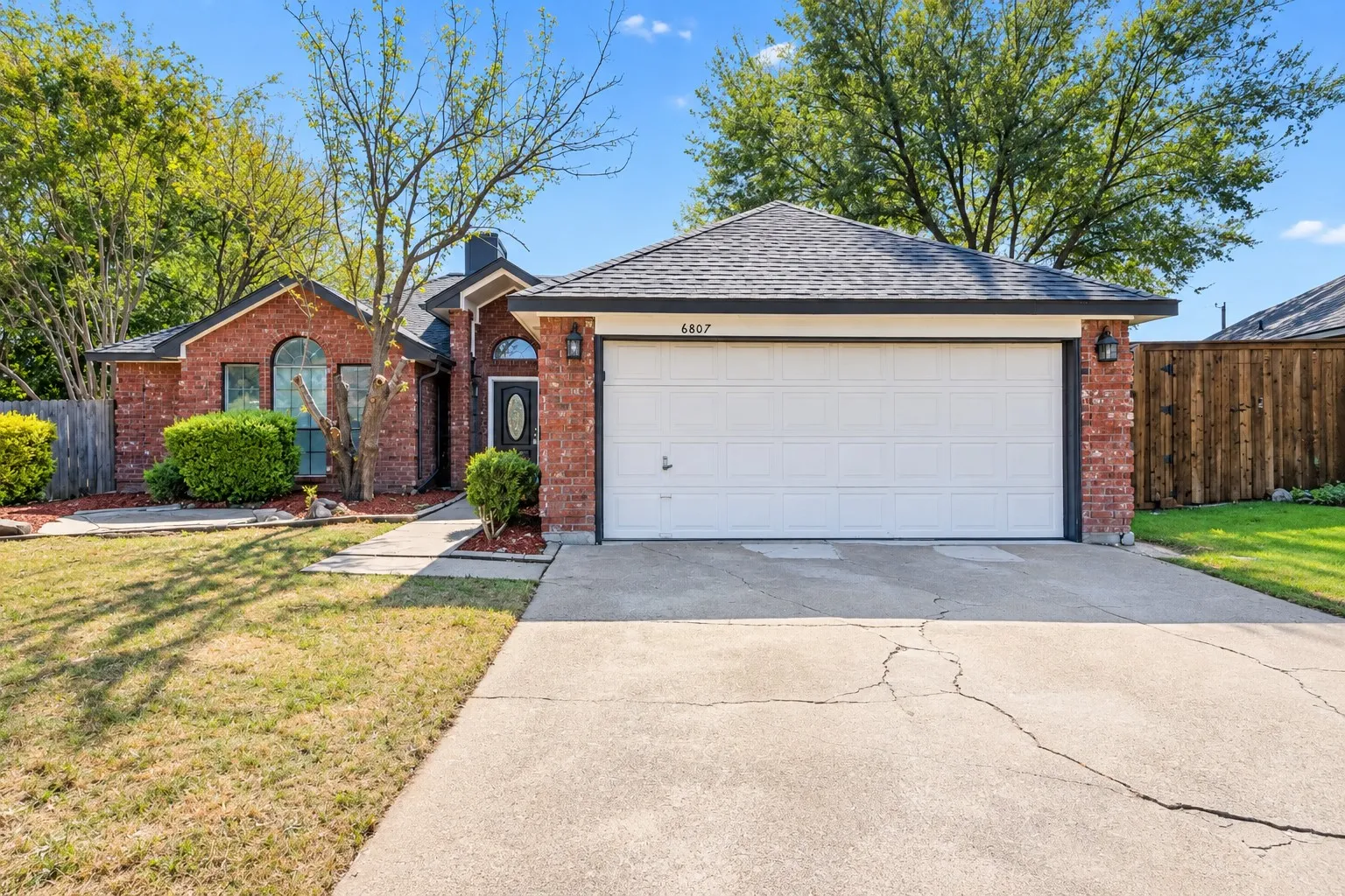 Brick facade with an attached two-car garage, prominent arched window, and a dark asphalt shingle roof