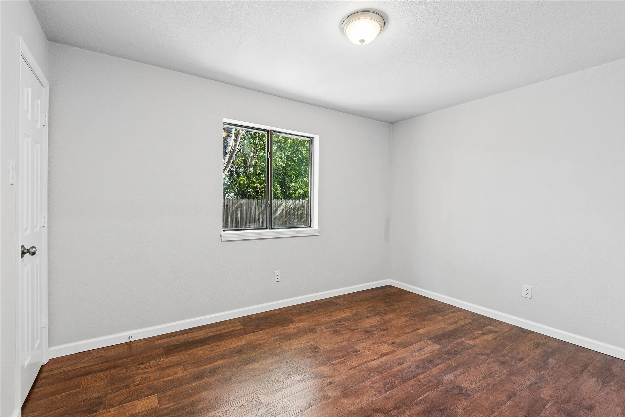 Wood-finish flooring, single window, flush-mount ceiling light fixture, neutral wall paint