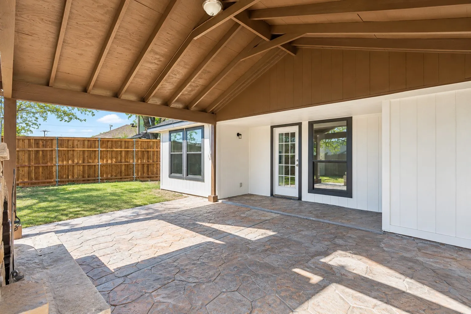 Covered patio featuring stamped concrete, exposed beam ceiling, and a glass-paneled door