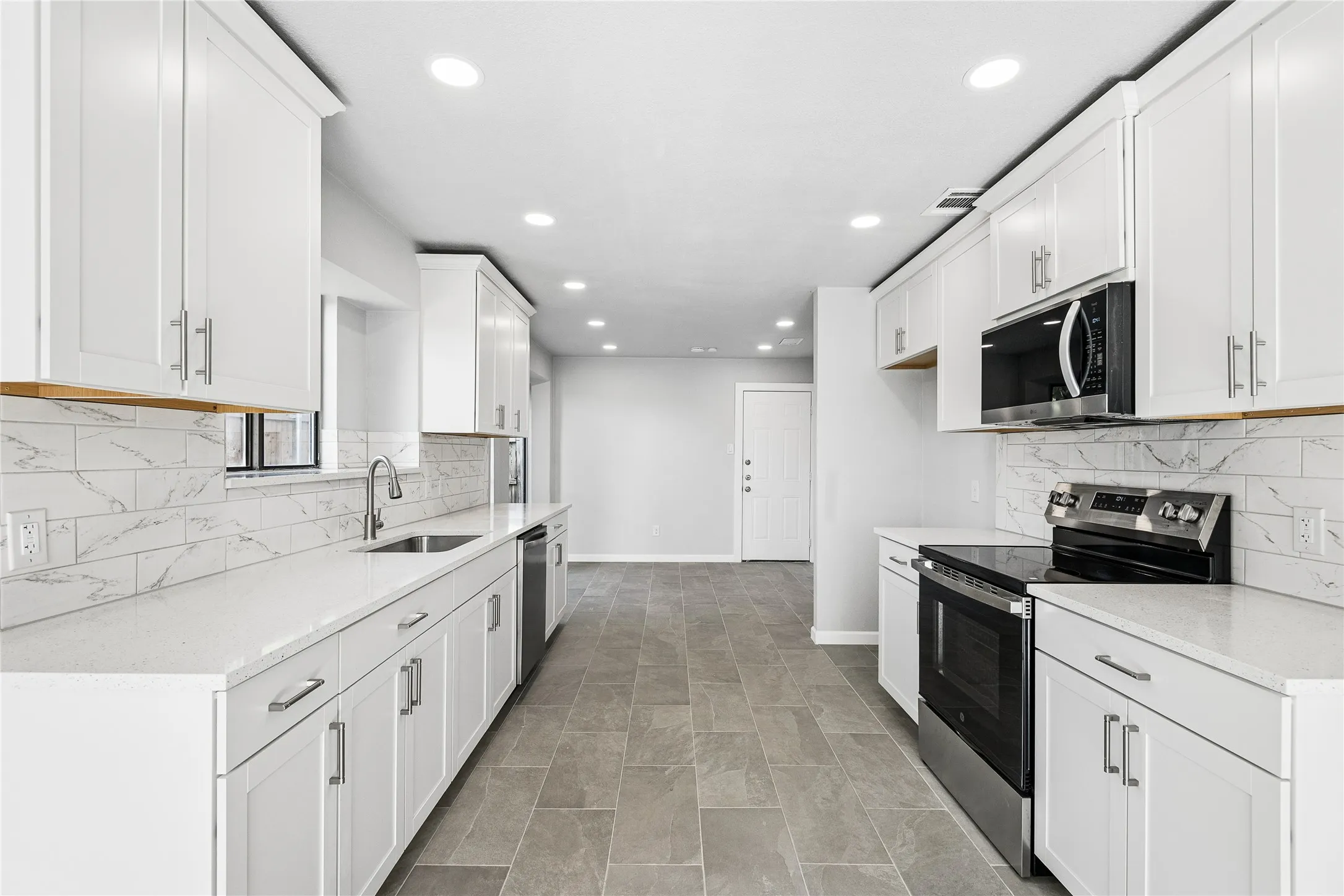 Modern kitchen featuring white shaker cabinetry, stainless steel appliances, marble-look subway tile backsplash, light-toned countertops, and recessed lighting