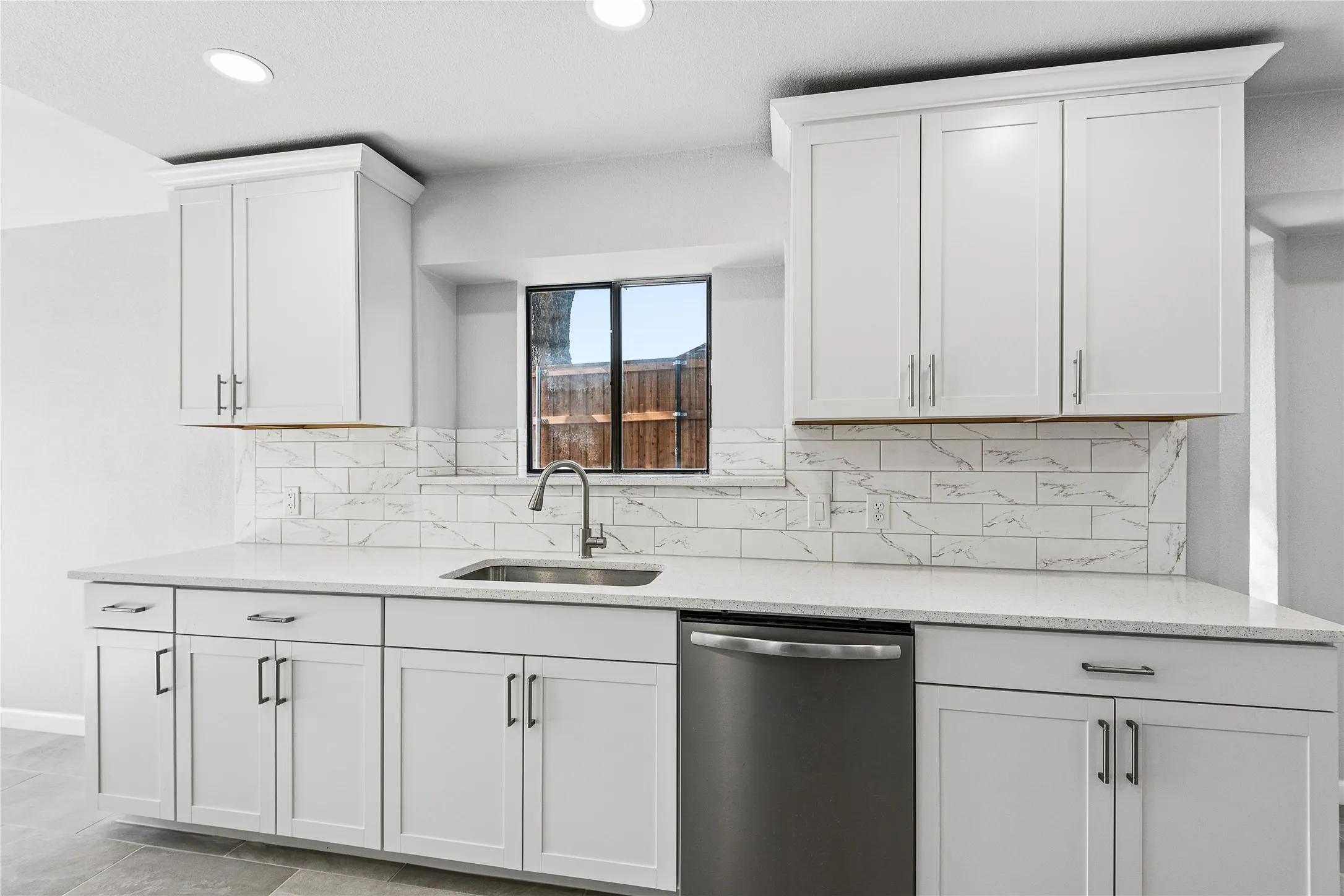 White shaker-style cabinetry with matte black hardware, white countertop, subway tile backsplash, and stainless steel sink