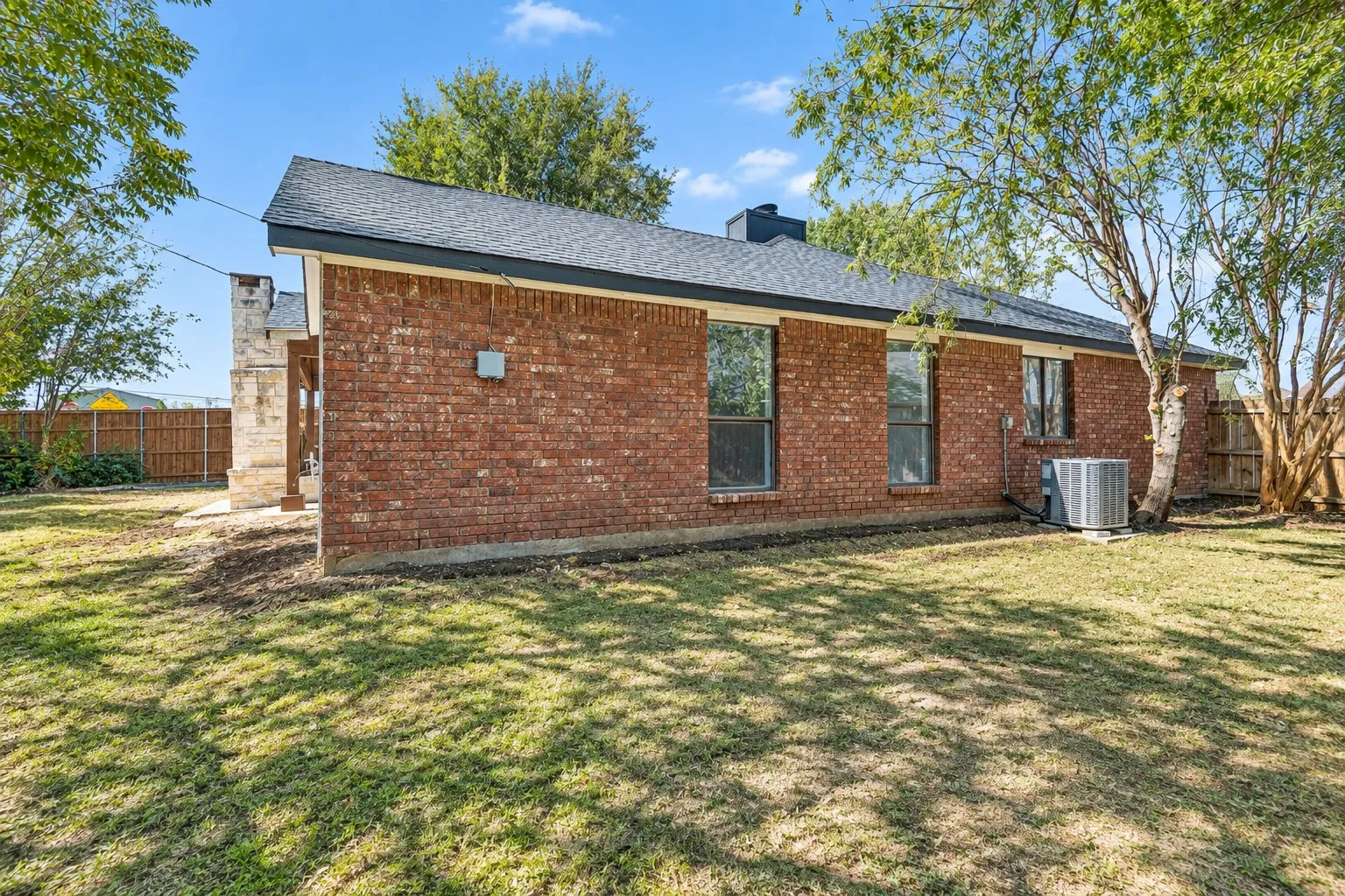 Brick exterior with multiple windows, a covered patio with wood posts, and an expansive lawn