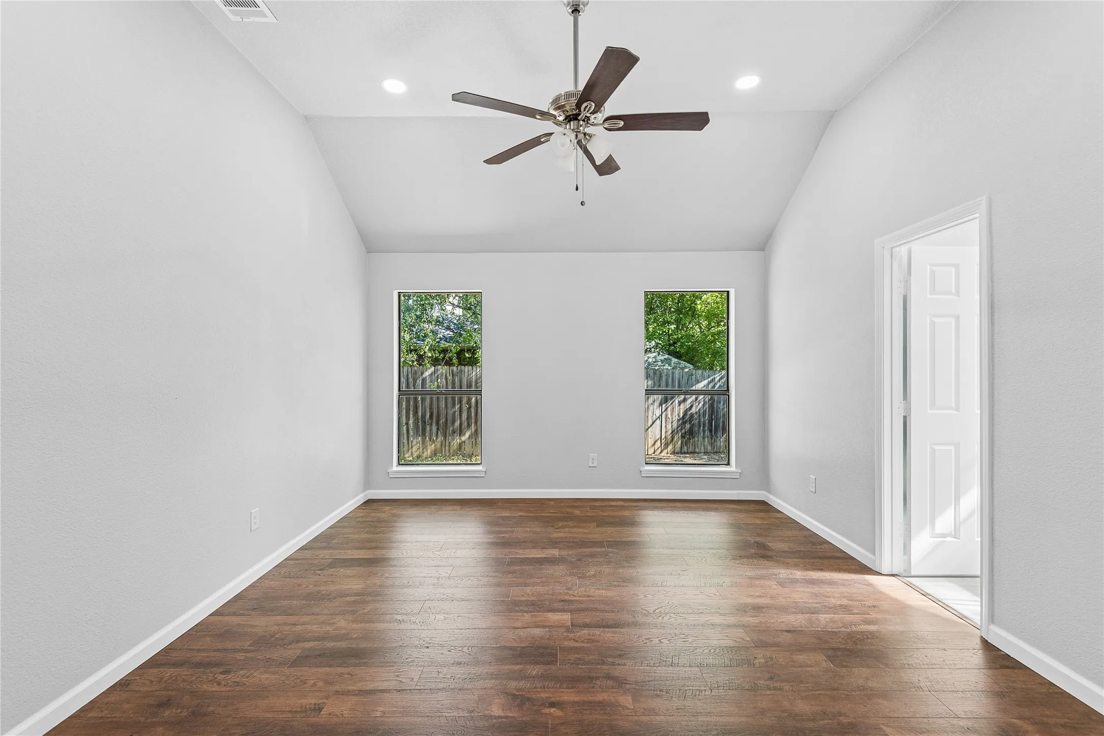 Vaulted ceiling with recessed lighting and a ceiling fan, wood-finish flooring, two rectangular windows, and a paneled door