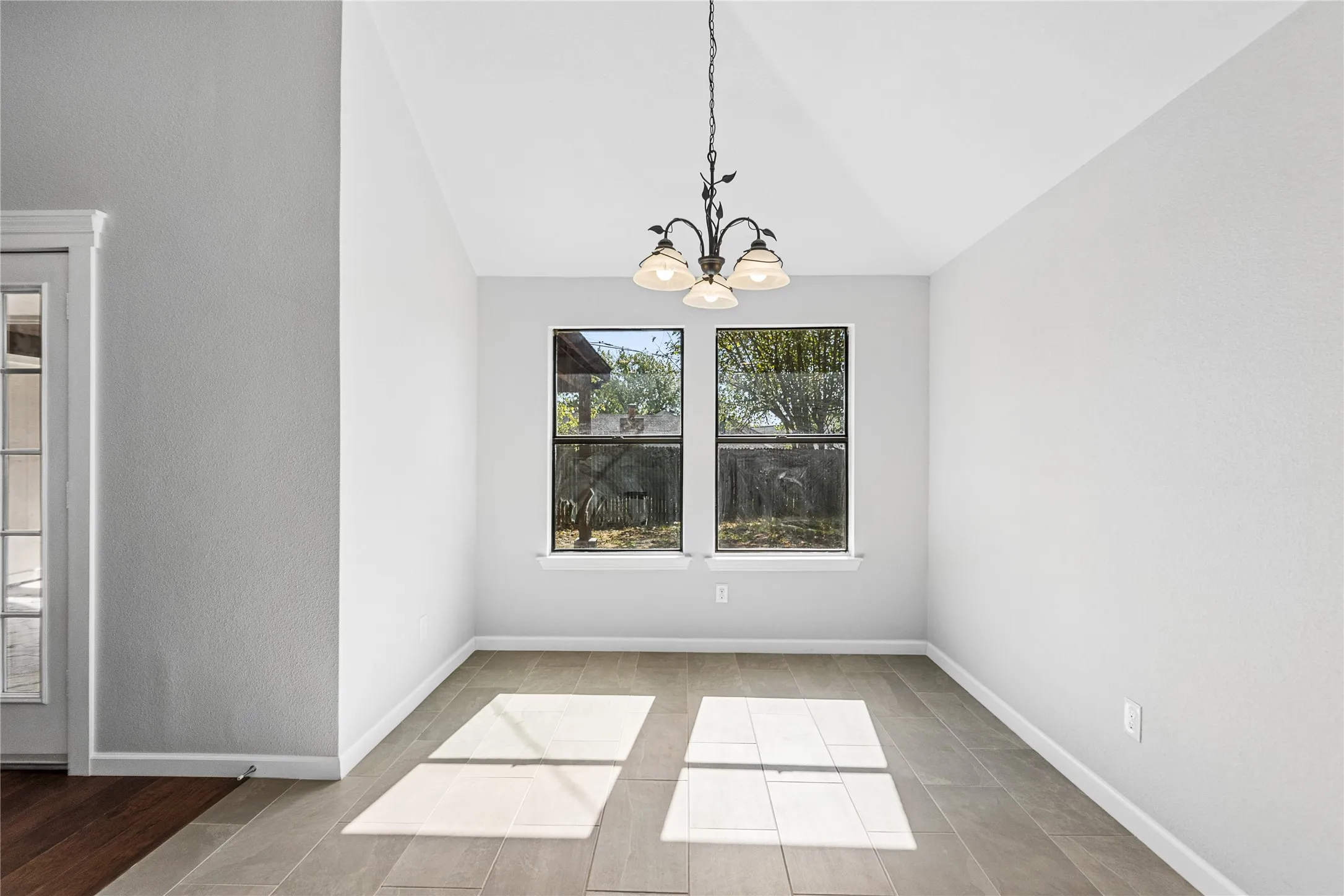 Vaulted ceiling with an ornamental chandelier, wood-finish flooring, and dual pane windows