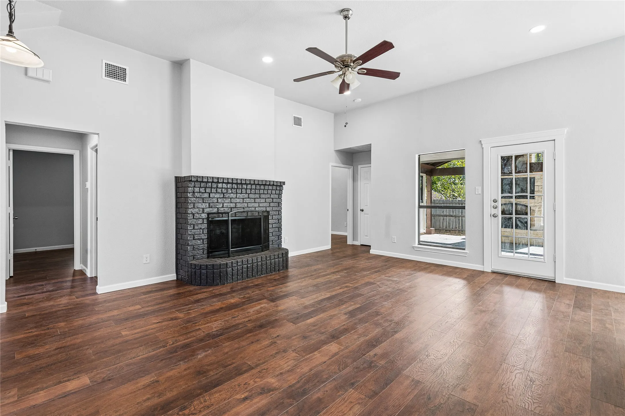 Vaulted ceilings, wood-finish flooring, a brick fireplace, a ceiling fan, and a glass-paneled exterior door