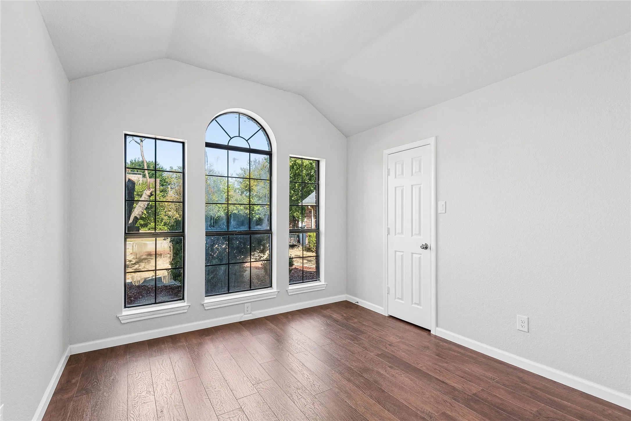Vaulted ceiling, wood-finish flooring, arched window, two rectangular windows, paneled interior door
