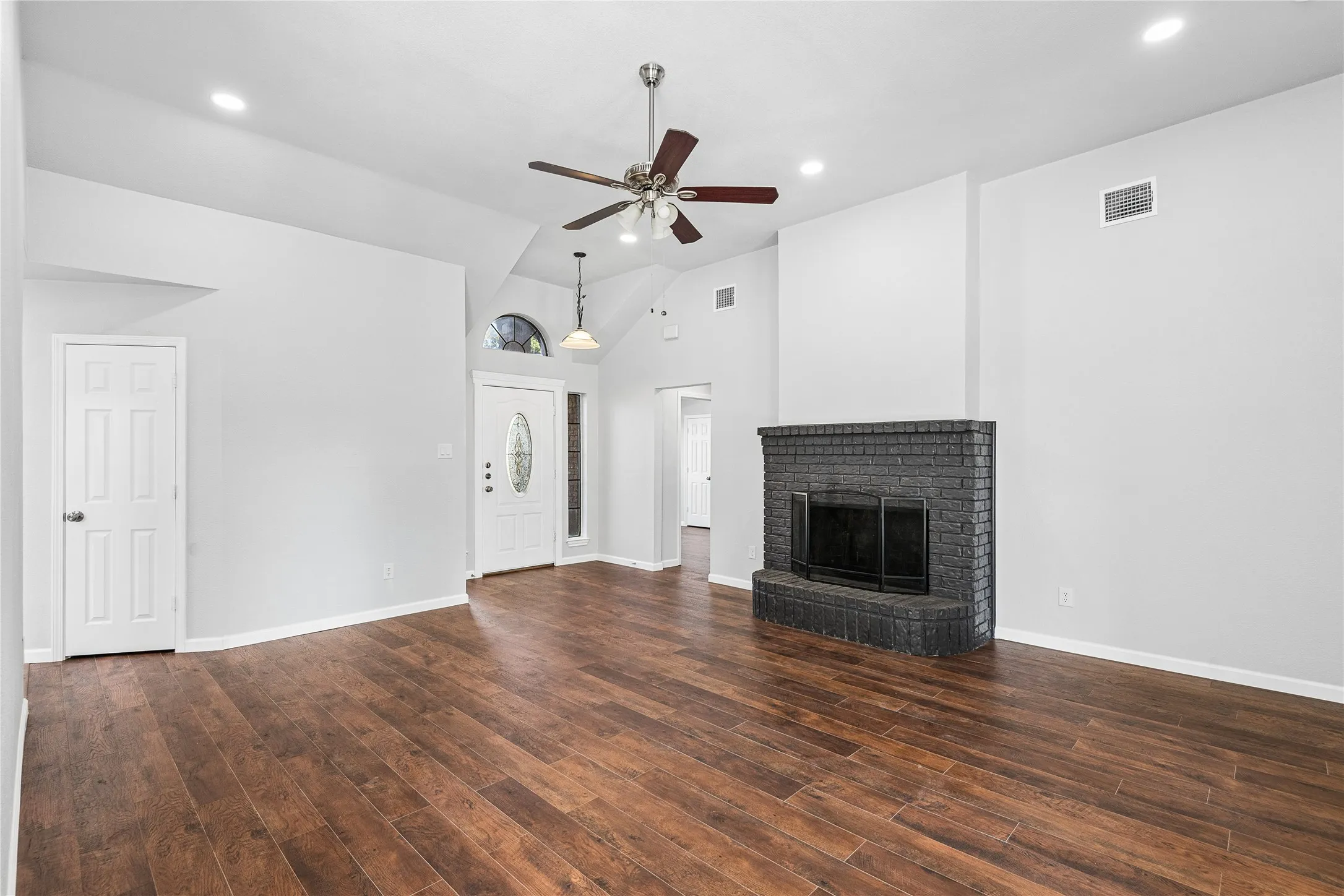 Spacious room featuring wood-finish flooring, a painted brick fireplace, a ceiling fan, recessed lighting, and a front entry door with a decorative glass insert and transom window