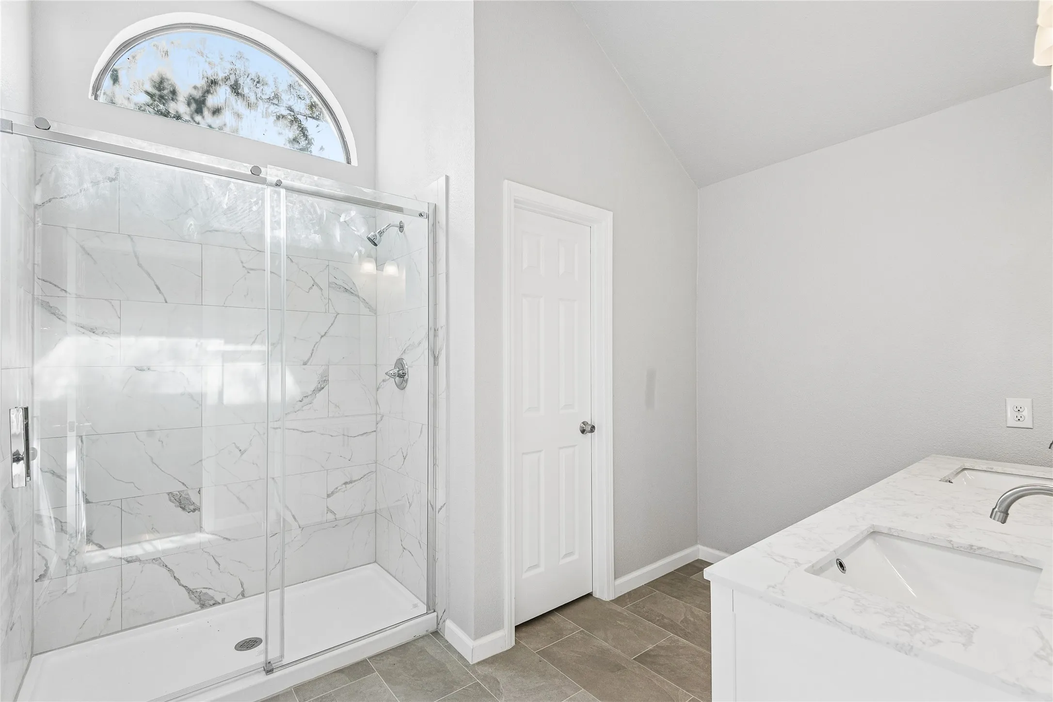 Walk-in shower with tile surround, semi-frameless glass enclosure, and an arched transom window