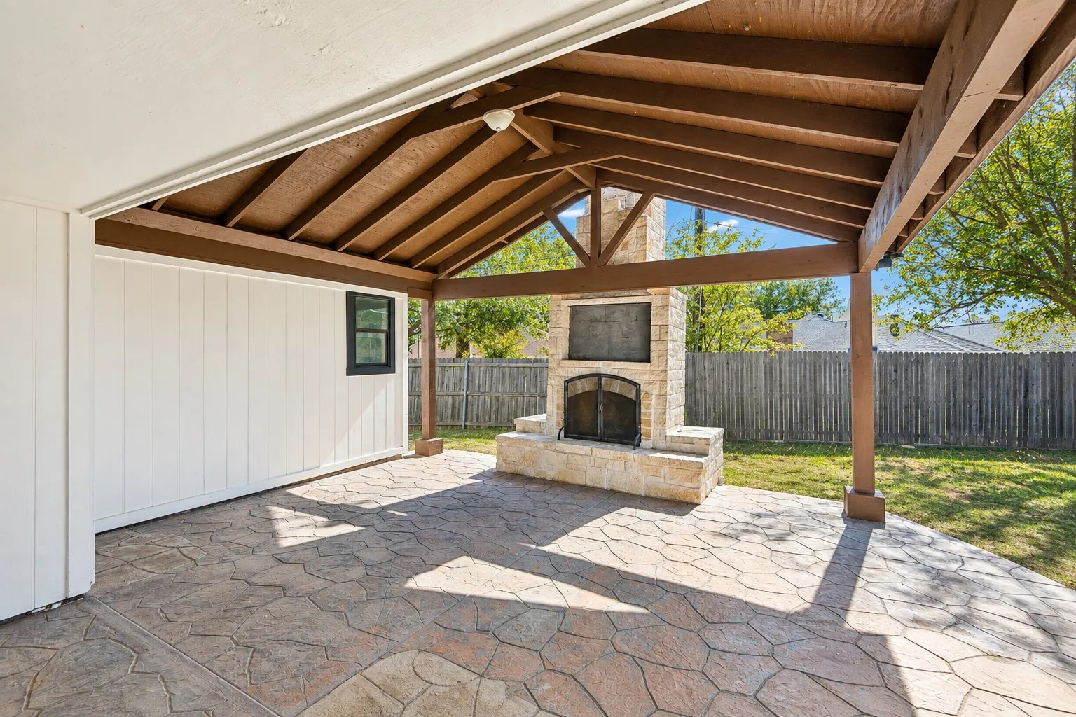 Covered patio featuring a stone fireplace, wood-beamed ceiling, and stamped concrete flooring