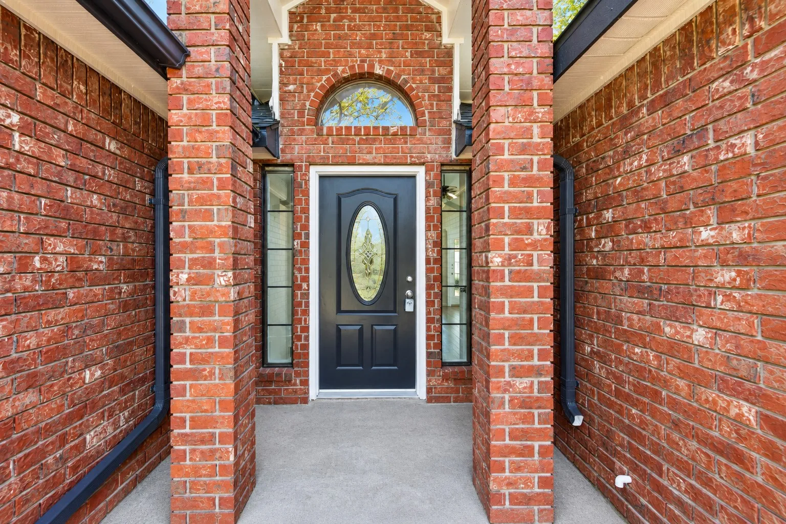 Brick exterior with a covered entry, dark paneled front door with oval glass insert, and transom window