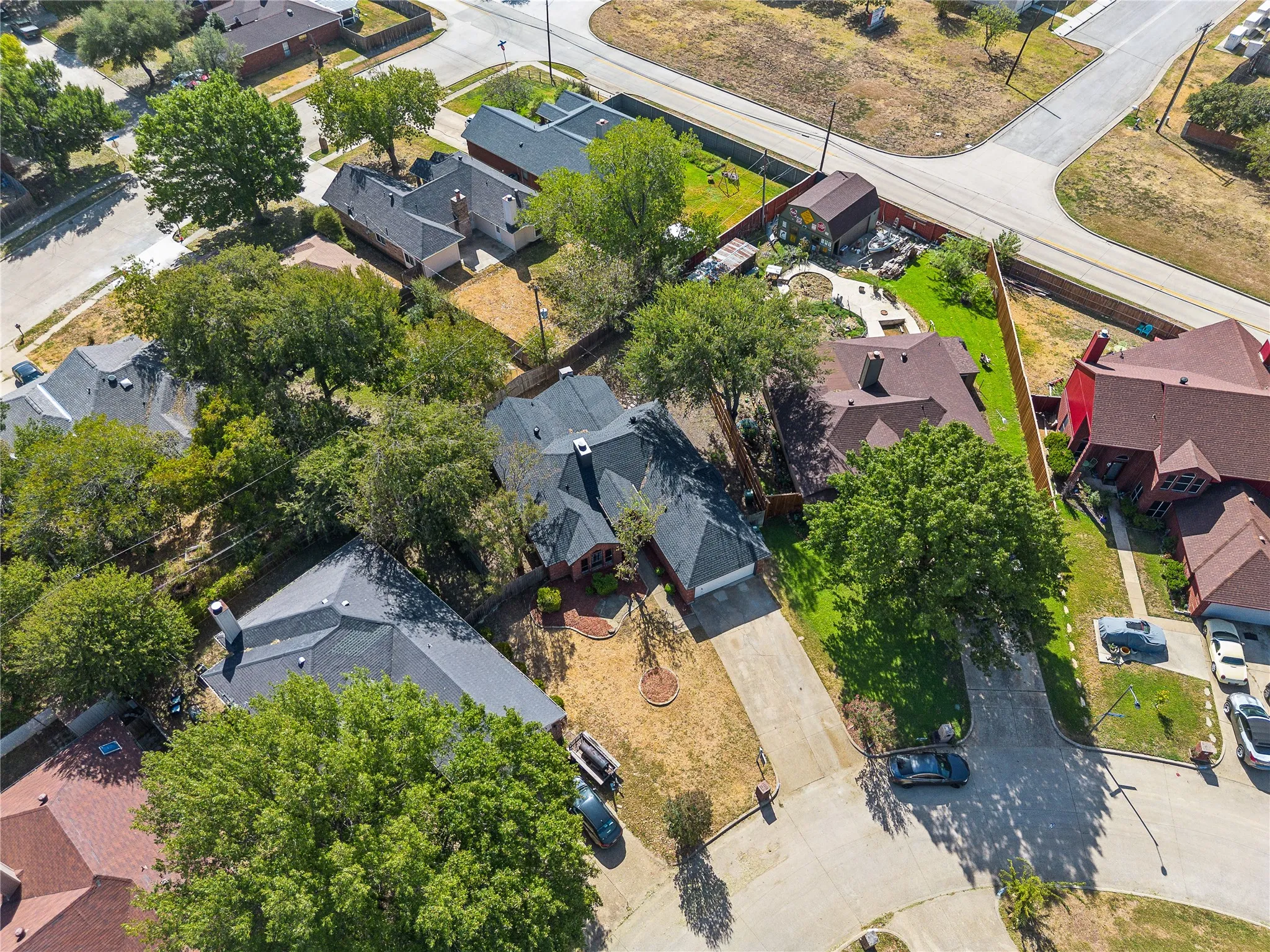 Aerial perspective of a neighborhood featuring multiple properties with mature trees and a residential street