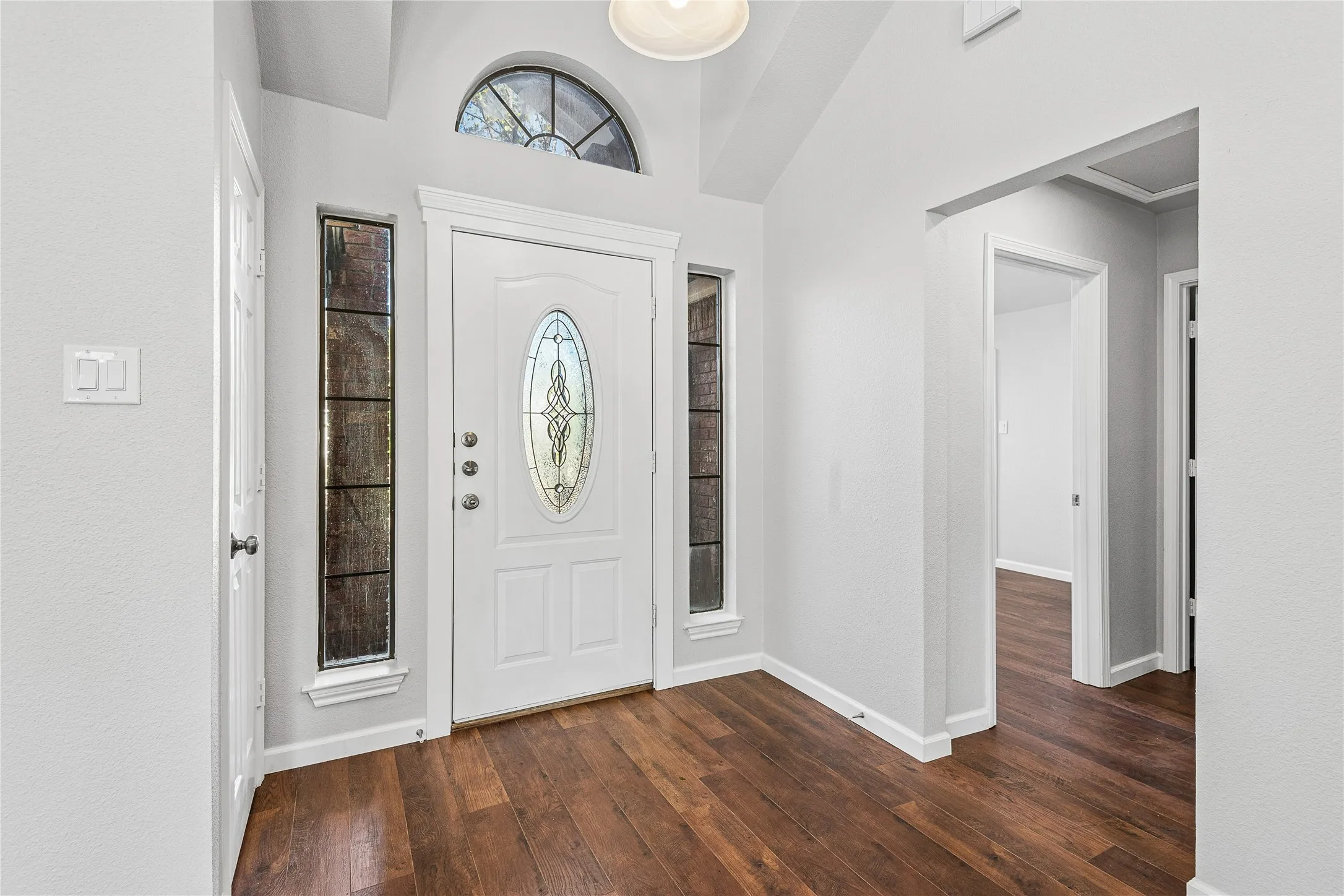 Entryway featuring wood-finish flooring, a white front door with an oval decorative glass insert, and a transom window above