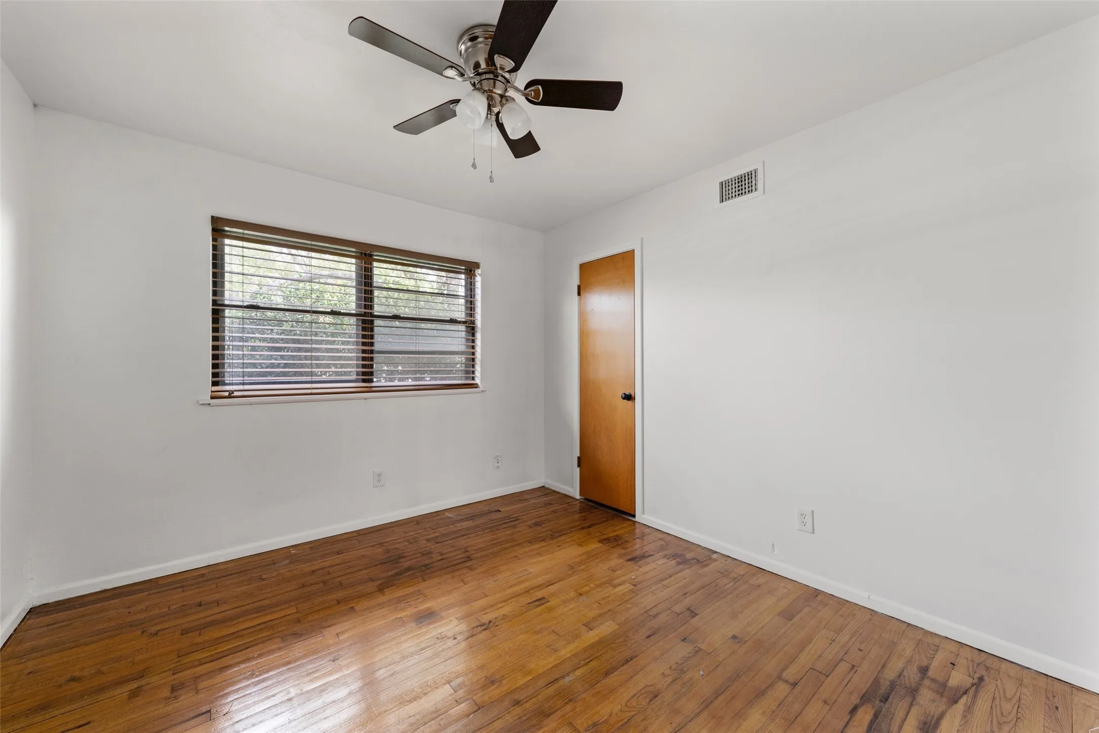 Hardwood flooring, window with blinds, ceiling fan with integrated lighting, and a wood-finish door