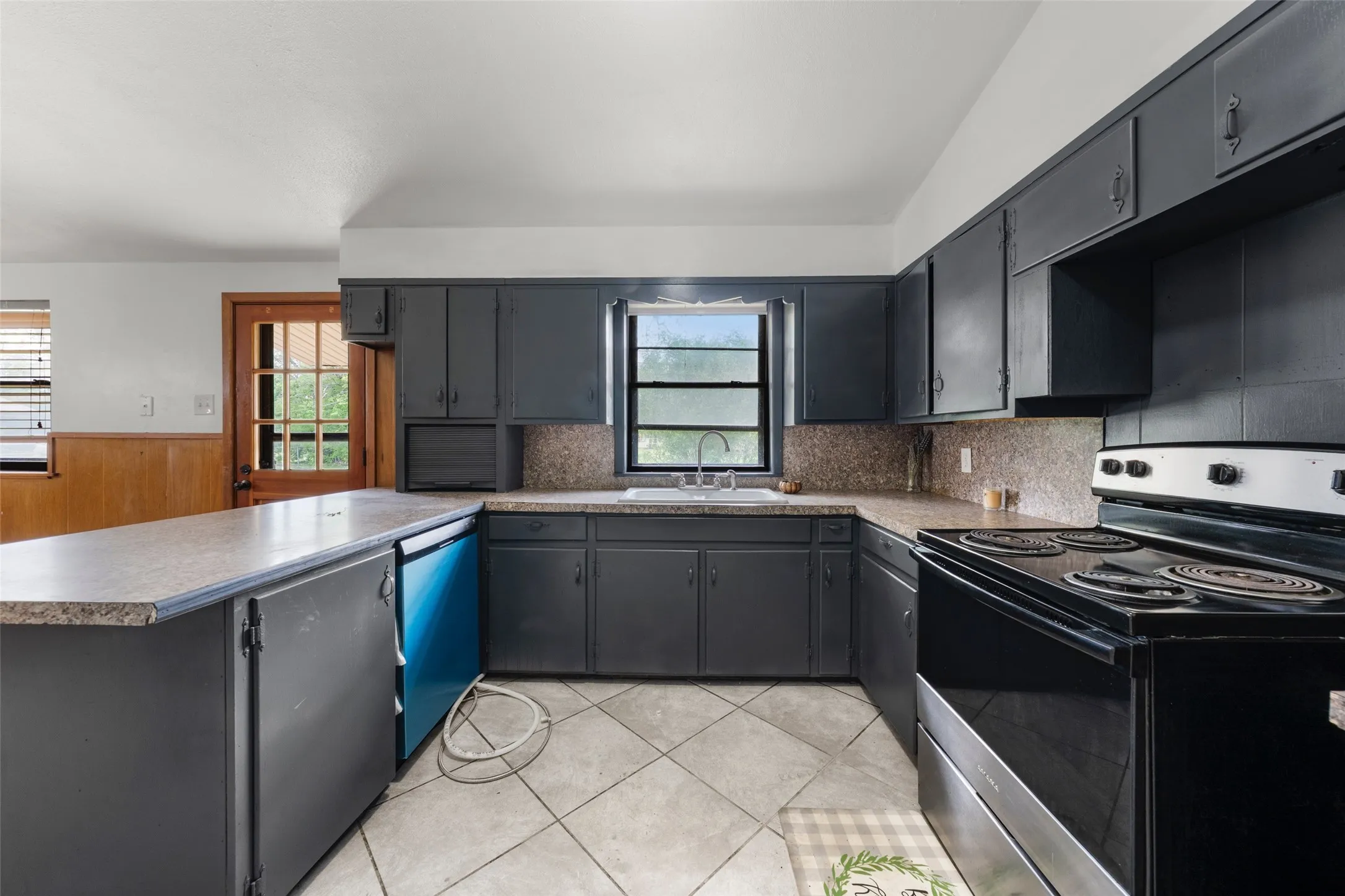 Kitchen featuring dark cabinetry, light-toned countertops, a built-in dishwasher, and a black electric range
