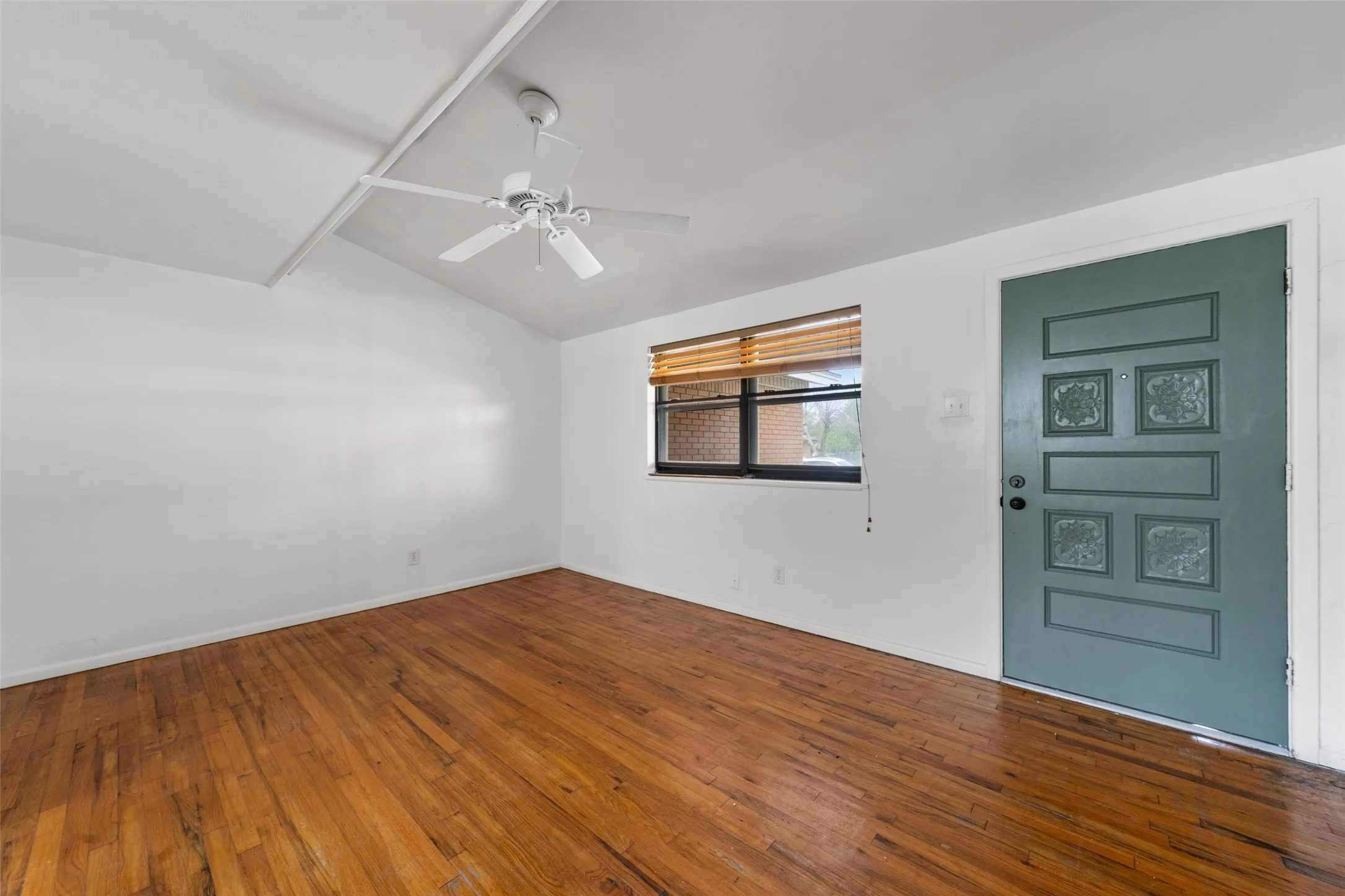 Vaulted ceiling, wood-finish flooring, ceiling fan, accent door with decorative panels, and a window with blinds