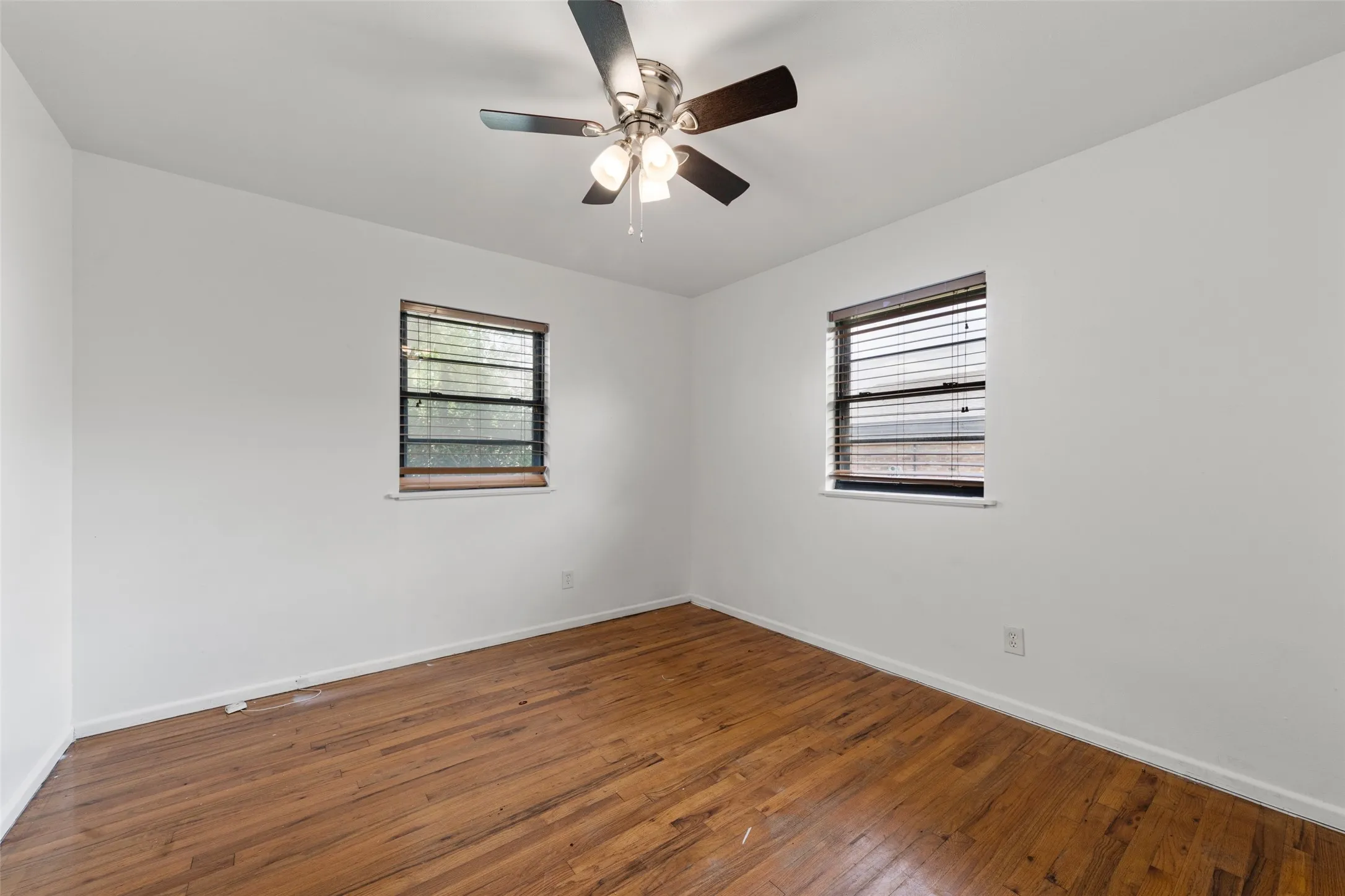Wood-finish flooring with white walls and dual windows featuring blinds