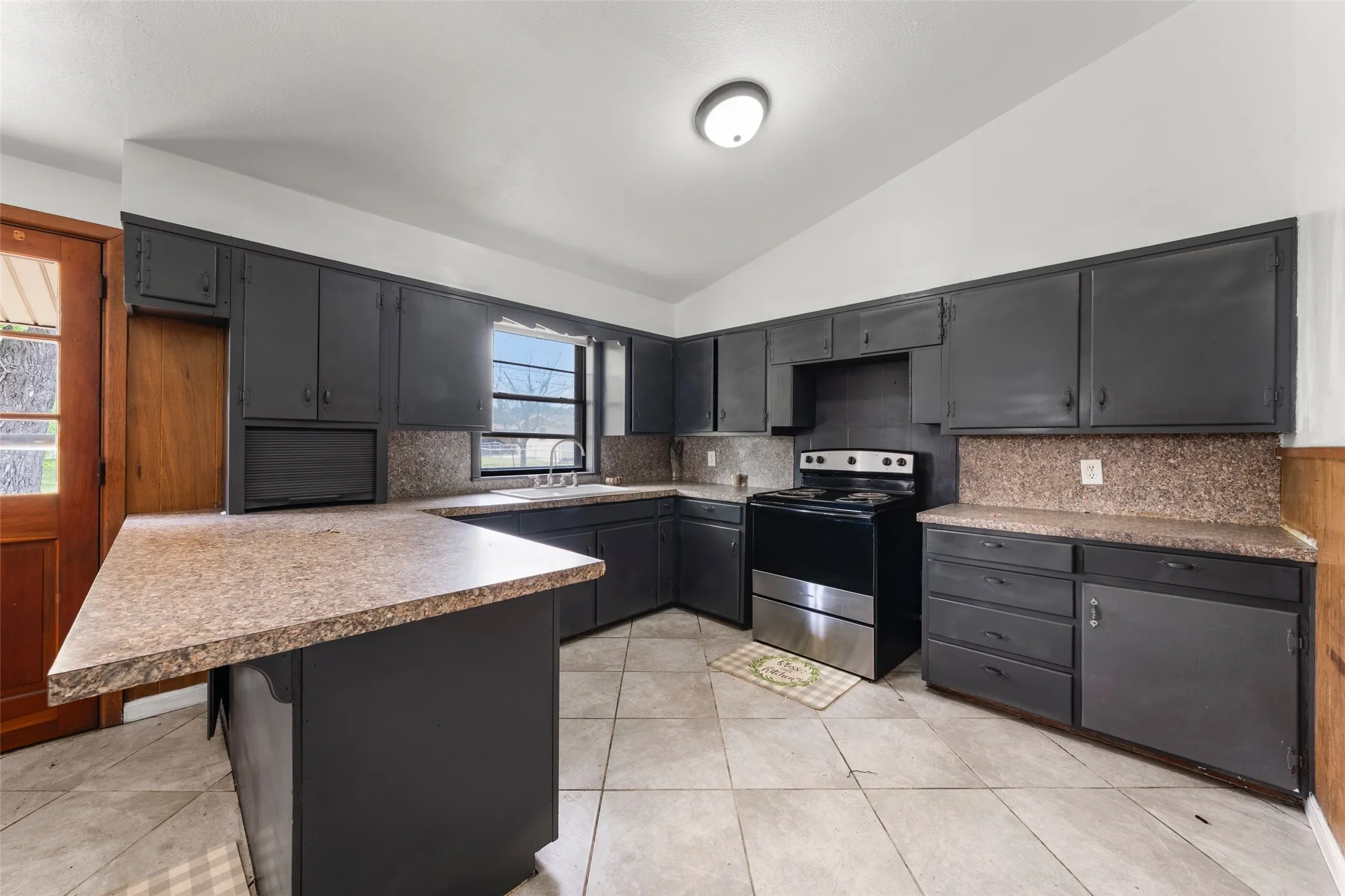 Kitchen featuring tile flooring, dark cabinetry, and a built-in electric range with stainless steel accents