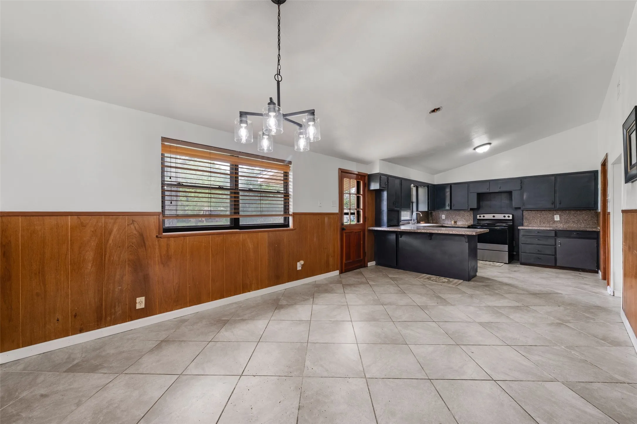 Spacious interior with vaulted ceilings, tile flooring, wood paneling, a kitchen island, and a modern chandelier