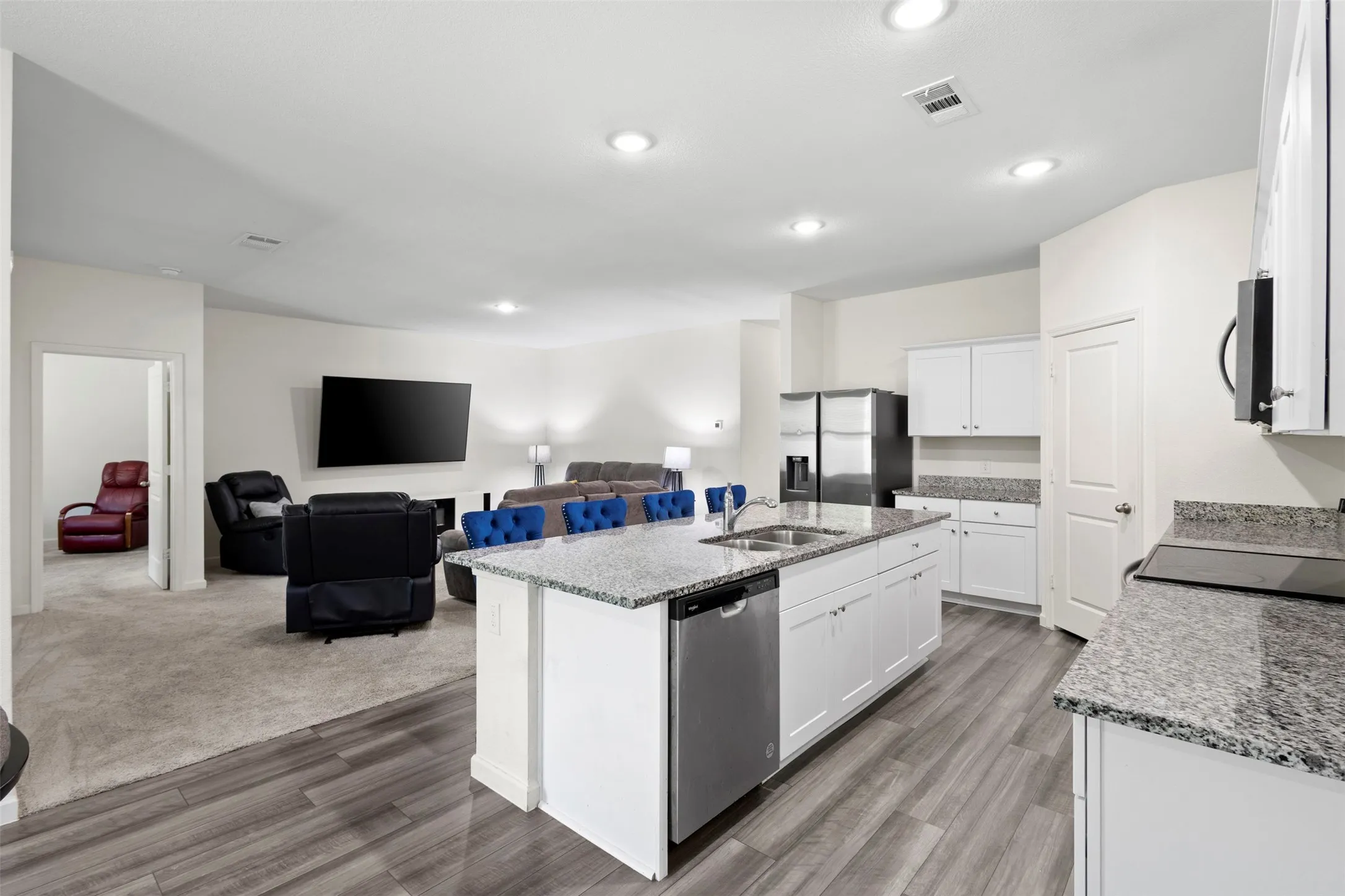 Kitchen featuring a large island with dual sinks, white cabinetry, stainless steel dishwasher, and stone countertops