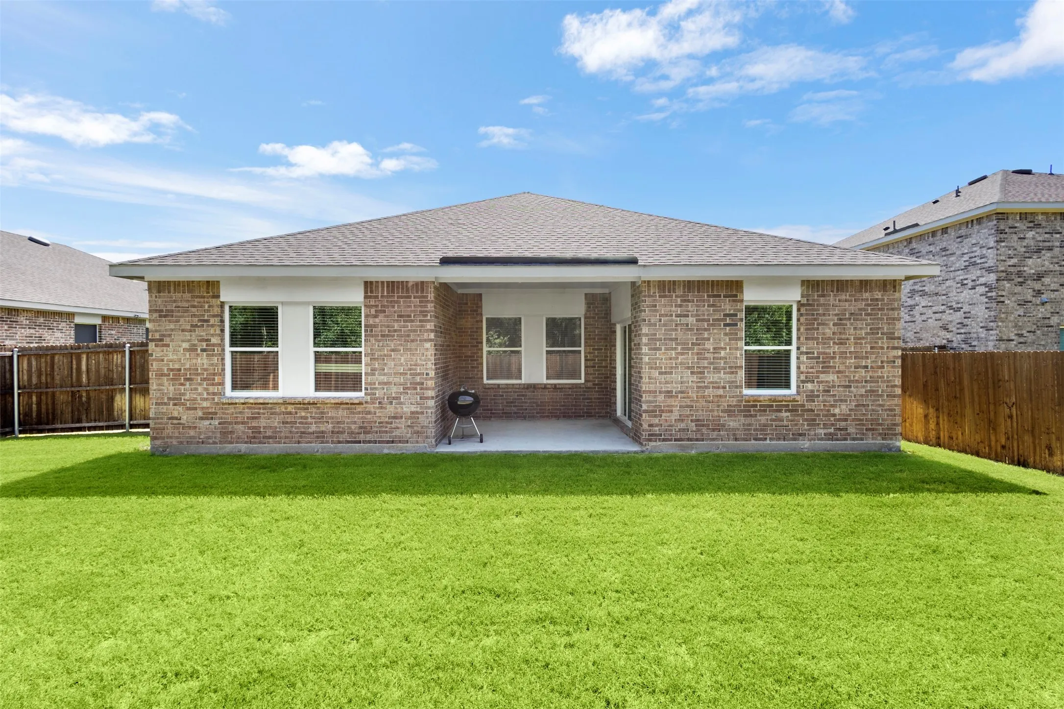 Brick exterior with multiple windows, covered patio, expansive lawn, and wood fencing