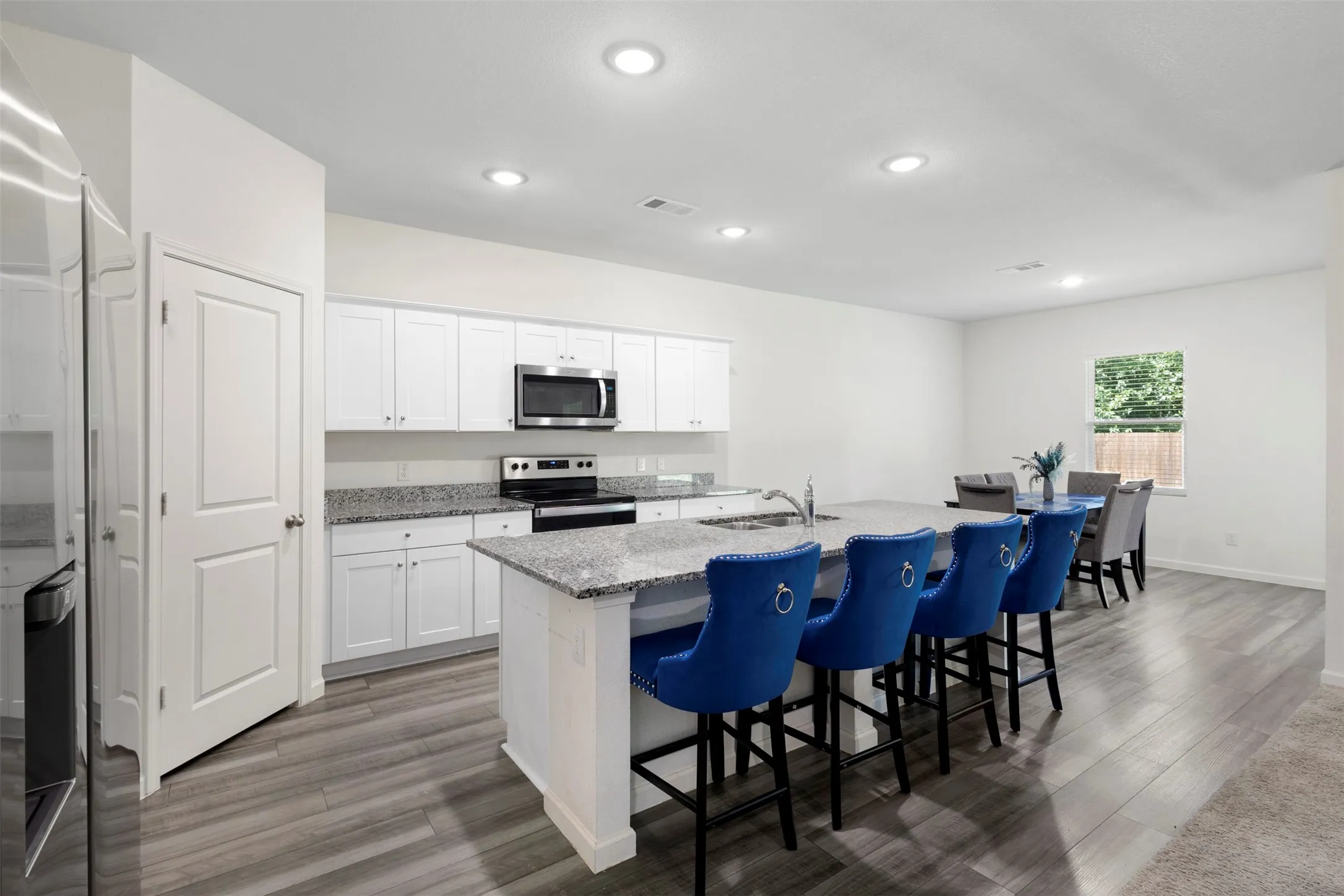 Kitchen featuring white cabinetry, stainless steel appliances, an island with seating, recessed lighting, and wood-finish flooring