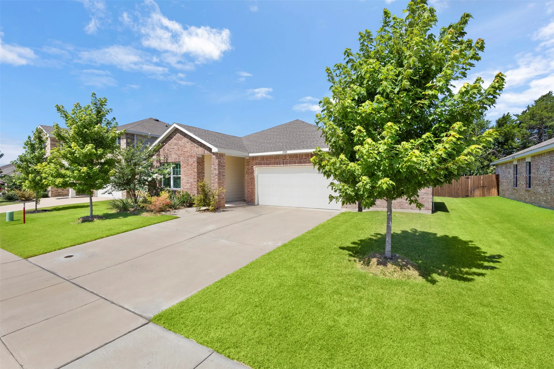 Brick exterior, attached garage, concrete driveway, front yard landscaping, and mature trees
