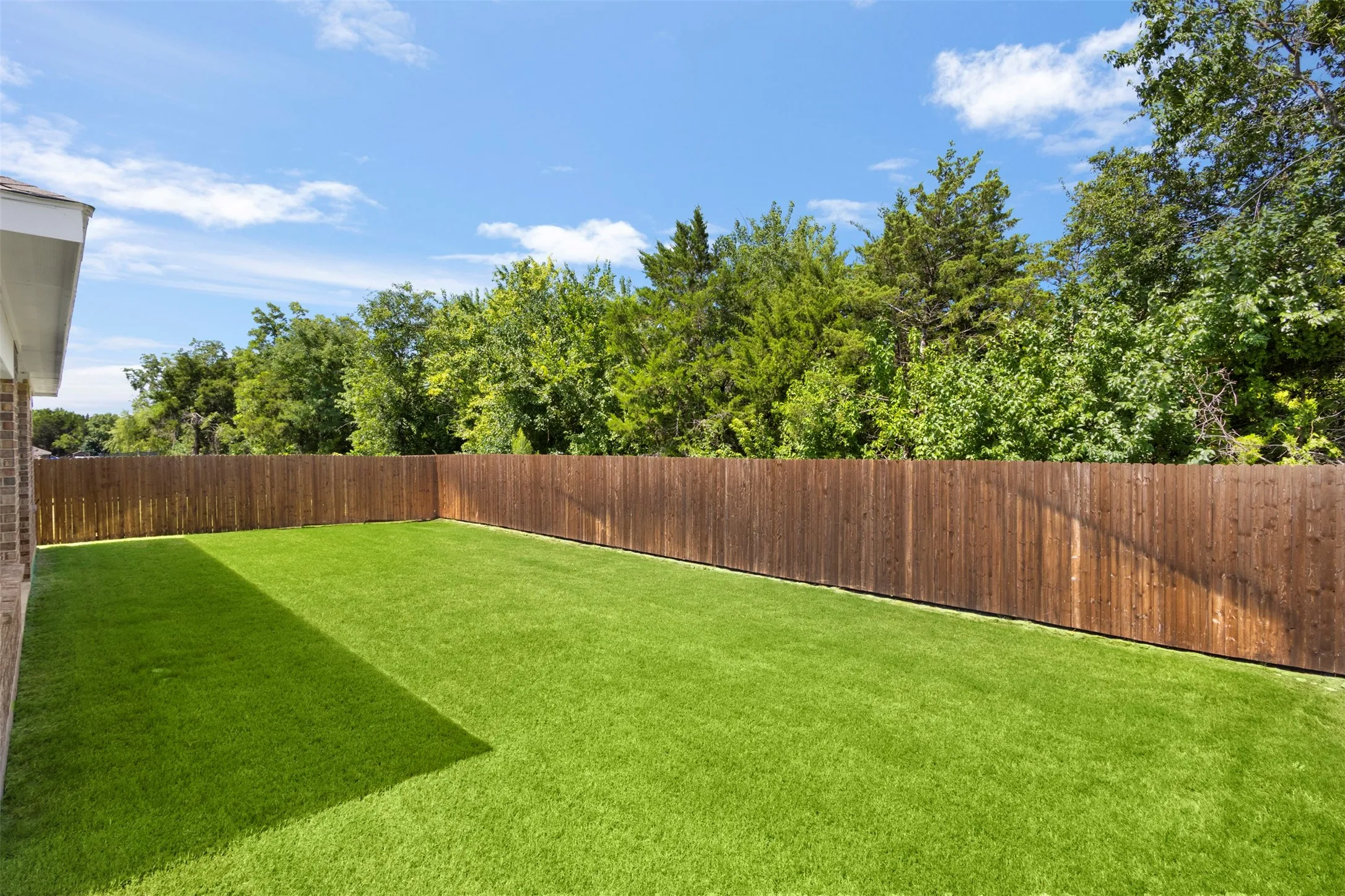 Expansive fenced backyard with artificial turf and mature perimeter trees