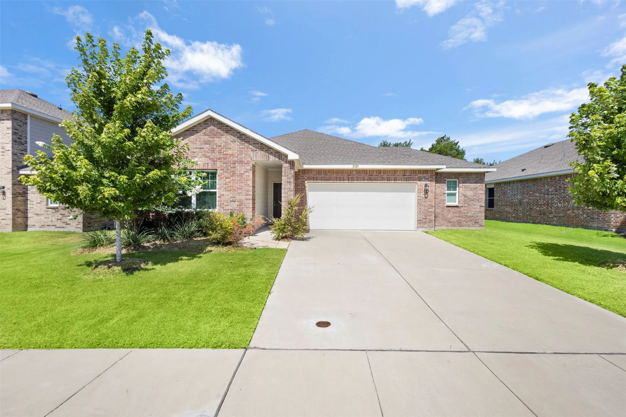 Brick exterior with white trim, attached two-car garage, concrete driveway, and front lawn