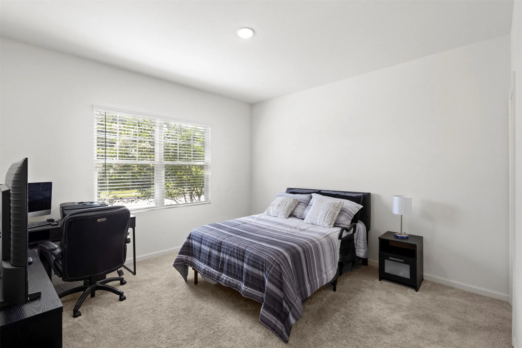 Recessed ceiling lighting, neutral carpeting, a large window with horizontal blinds, and light-toned walls