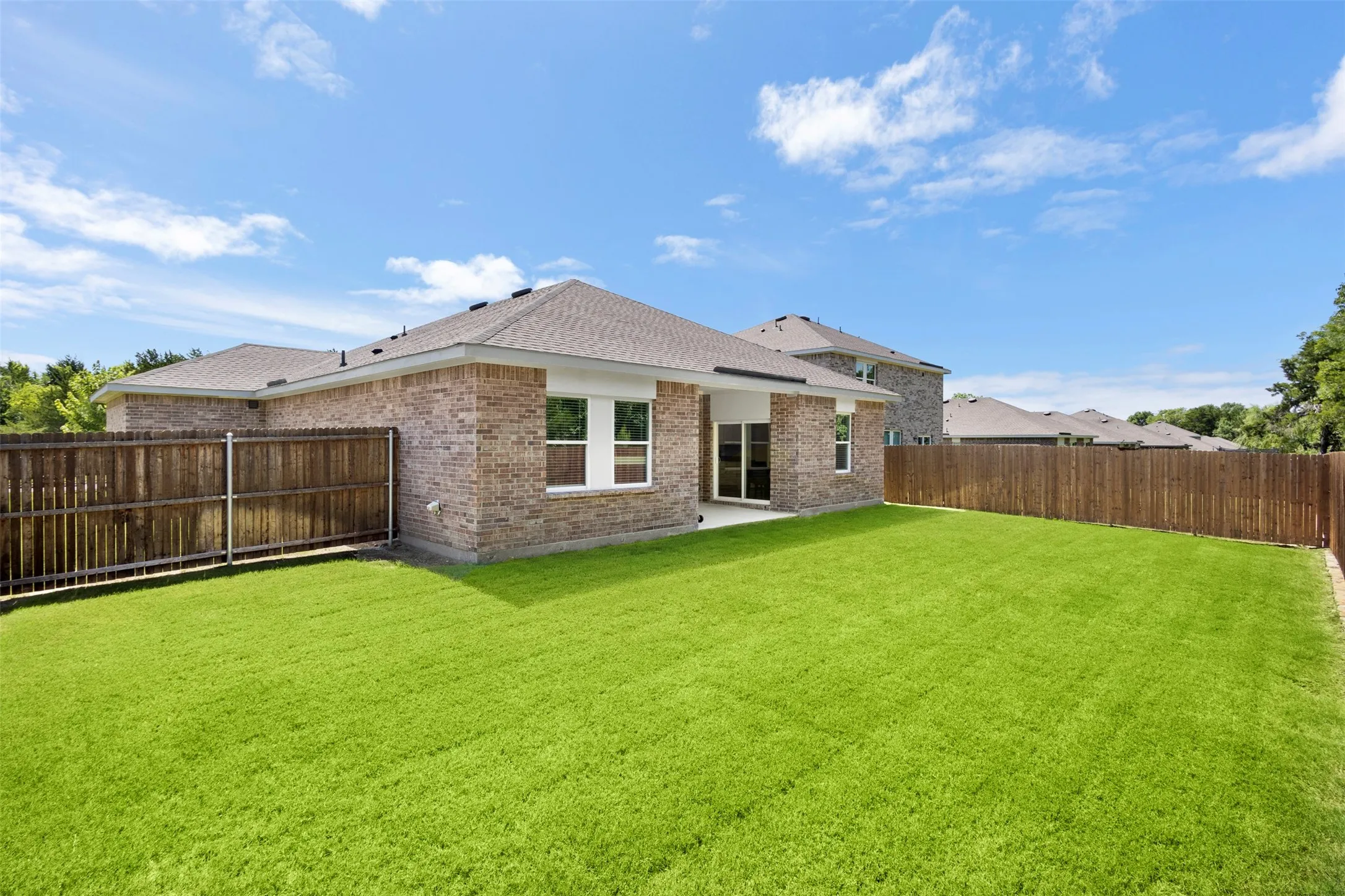 Expansive backyard featuring a manicured lawn, brick exterior, and a privacy fence