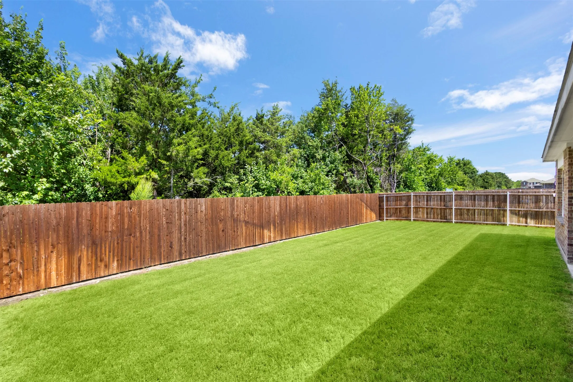 Expansive backyard featuring a lush lawn, wood fencing, and mature perimeter trees