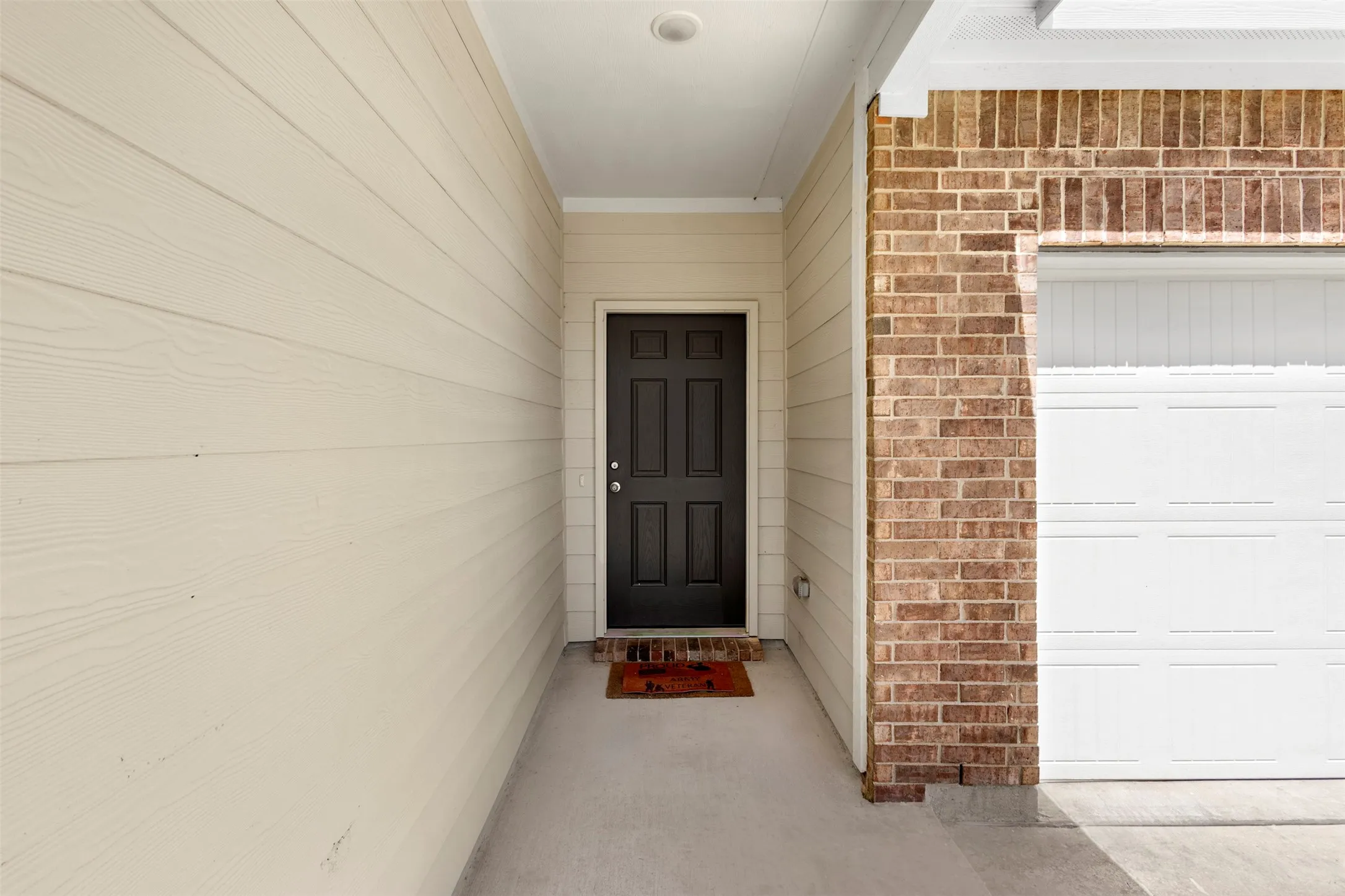 Brick and siding exterior with a black panel door, covered entry, and an attached garage