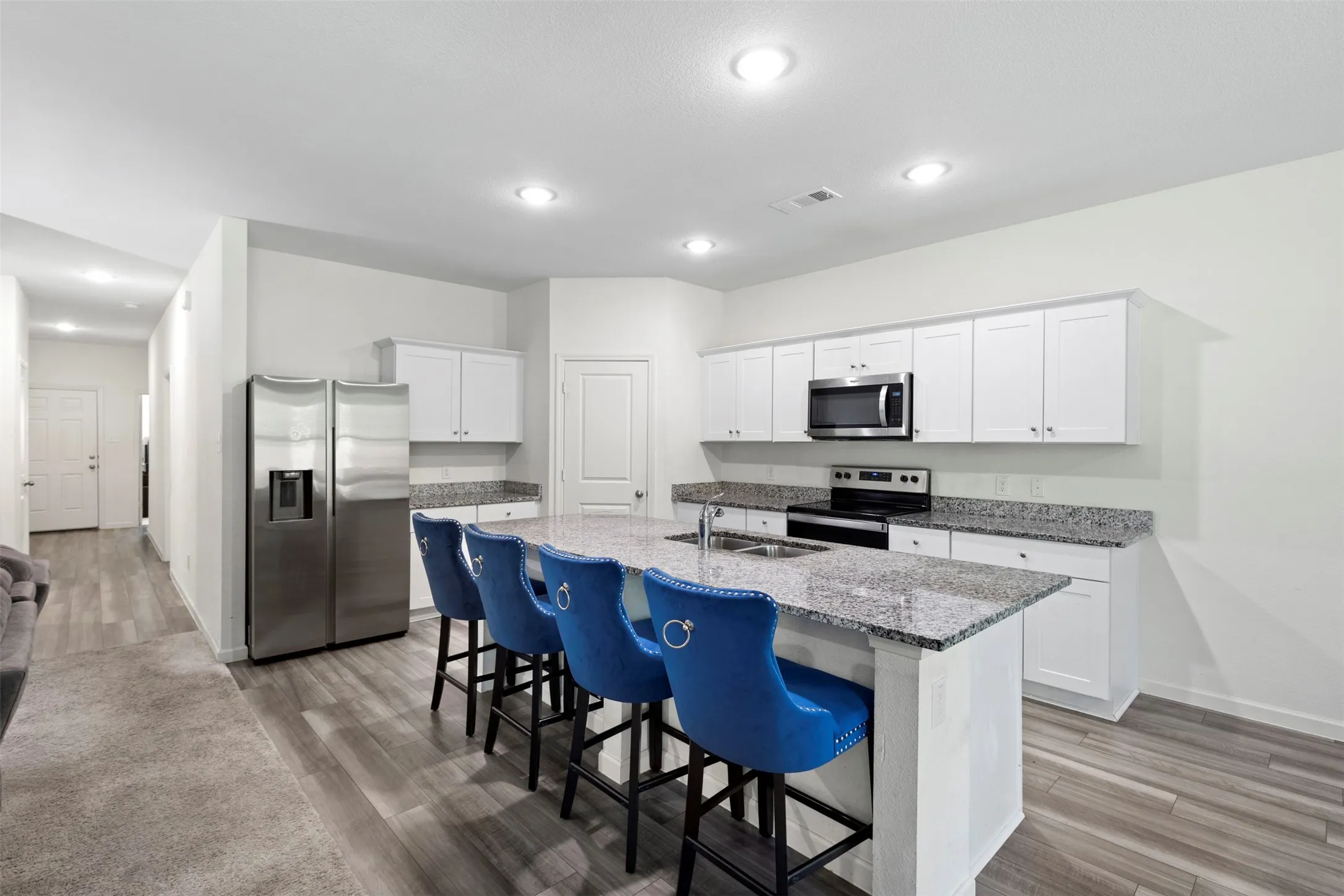 Kitchen featuring an expansive island with a dual-basin sink, white cabinetry, stainless steel appliances, and recessed lighting