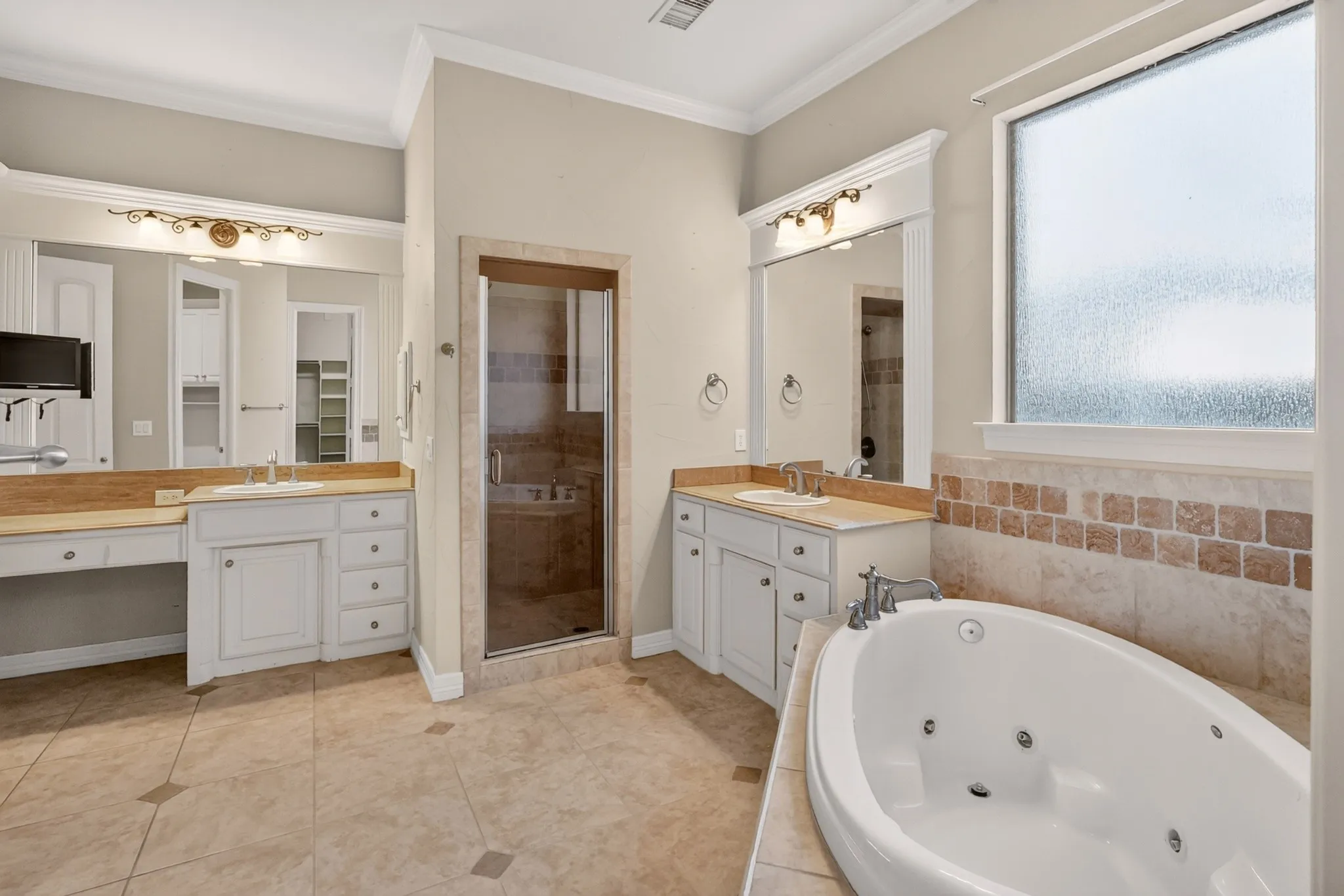 Primary Ensuite. Dual vanity with light-colored cabinetry, built-in soaking tub, tiled shower enclosure with glass door, and patterned tile flooring