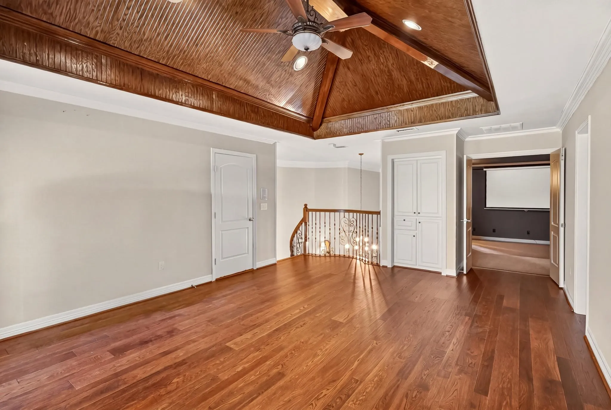 Expansive game room with wood finished flooring, vaulted wood-paneled ceiling, ceiling fan, and white built-in cabinetry. Attached media room.
