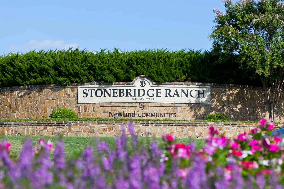 Stonebridge Ranch entry monument featuring stone cladding, integrated signage, and lush landscaping with mature shrubs and flowering plants