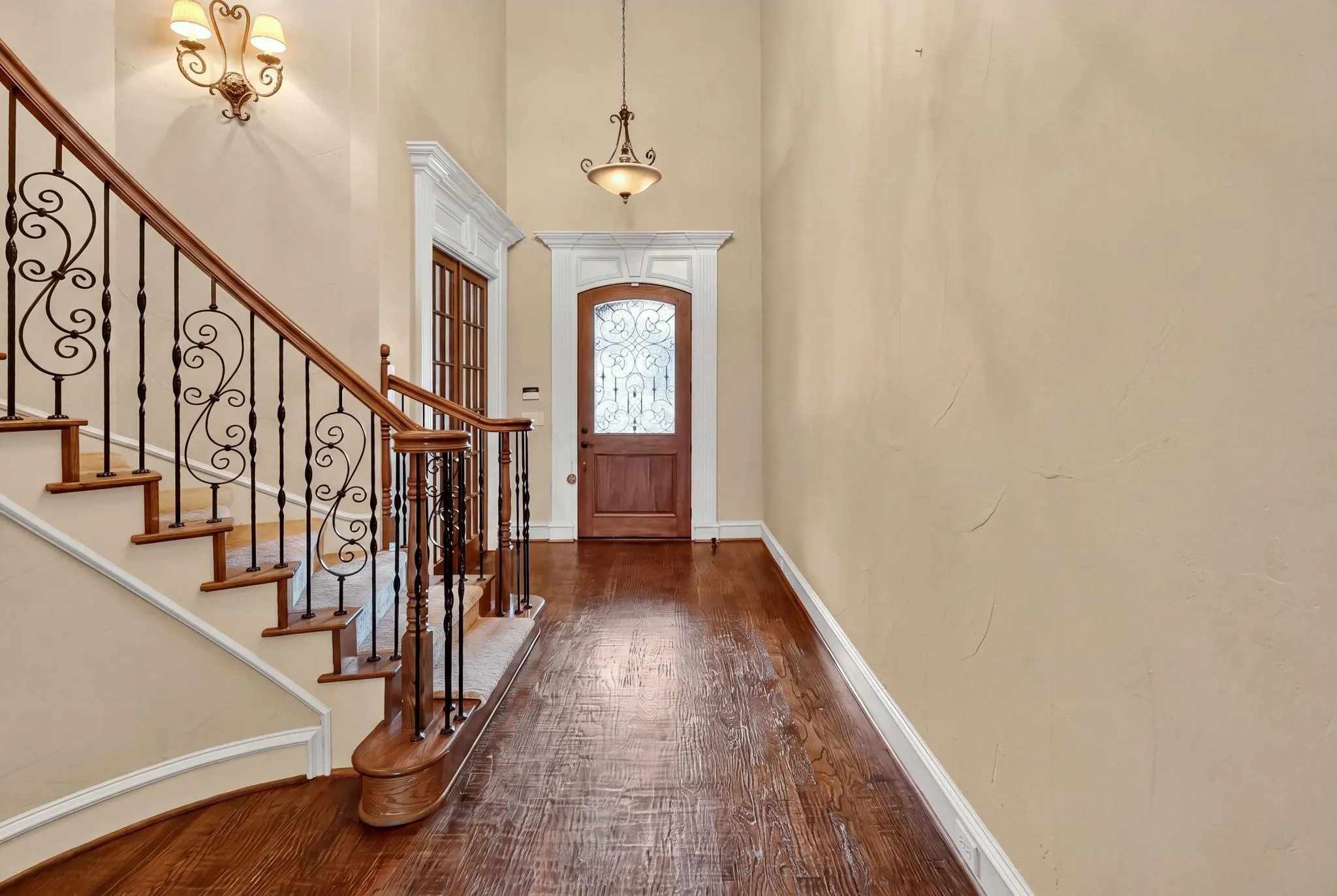 Hardwood flooring, curved staircase with wrought iron balusters, elegant entry door with decorative glass, and crown molding