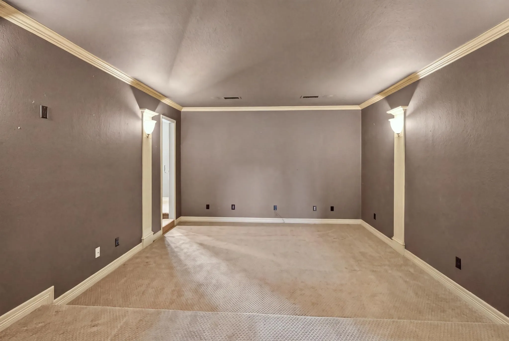 Spacious media room featuring wall-to-wall carpeting, crown molding, and decorative wall sconces