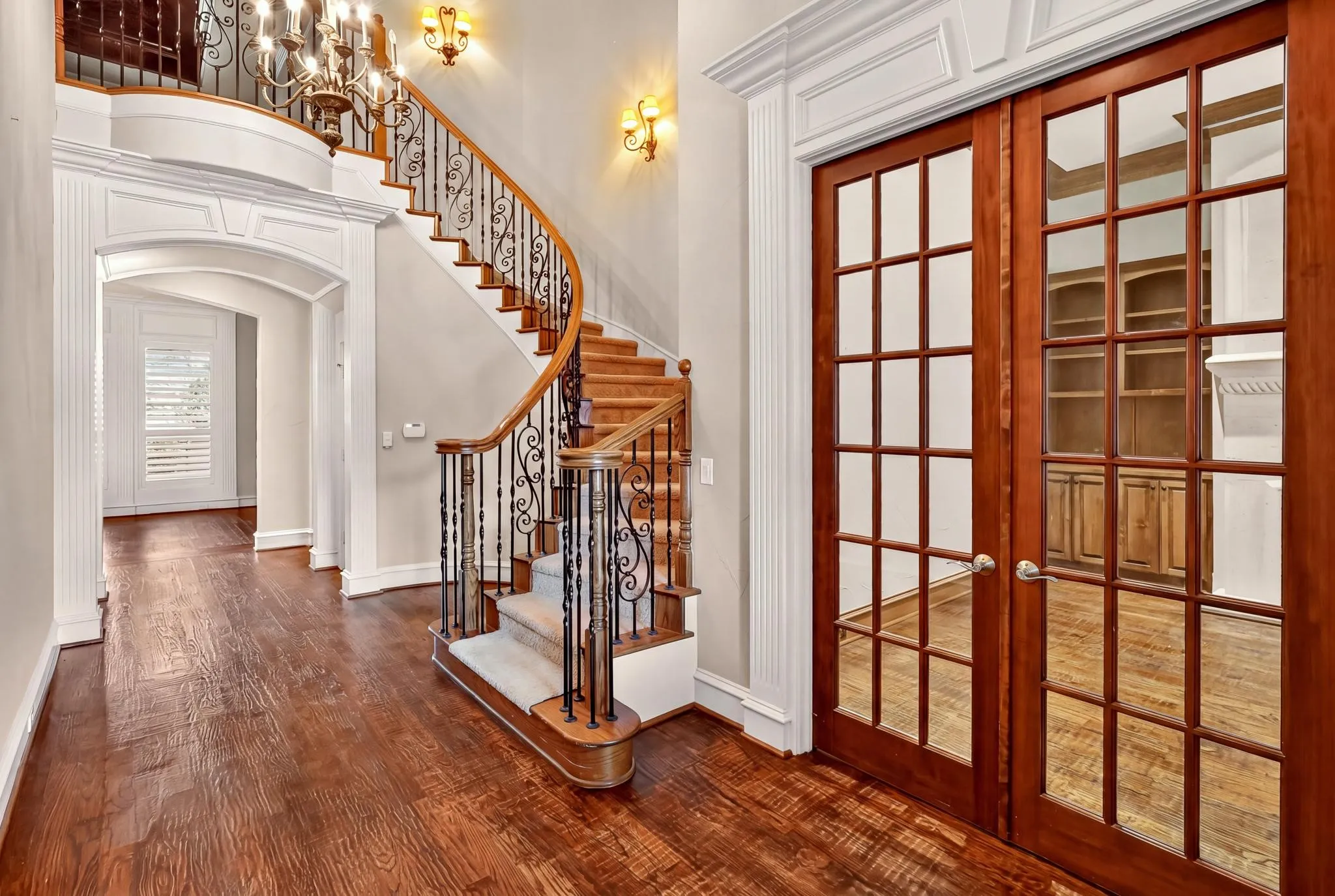 Gracious entry featuring wood-finish flooring, a grand curved staircase with wrought iron balusters, and elegant archways