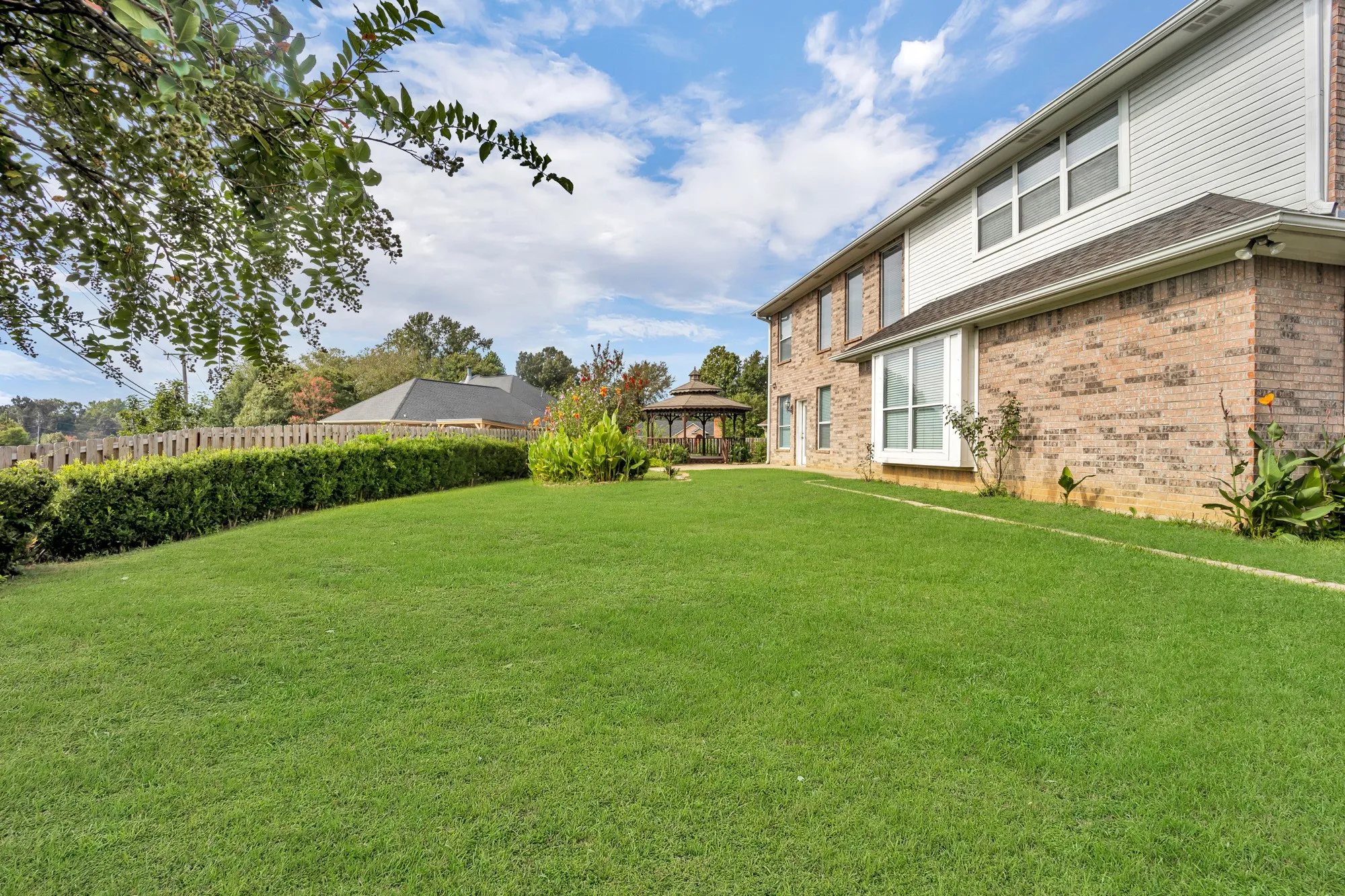 Expansive lawn area with a hedge border, a wooden fence, and a gazebo in the background