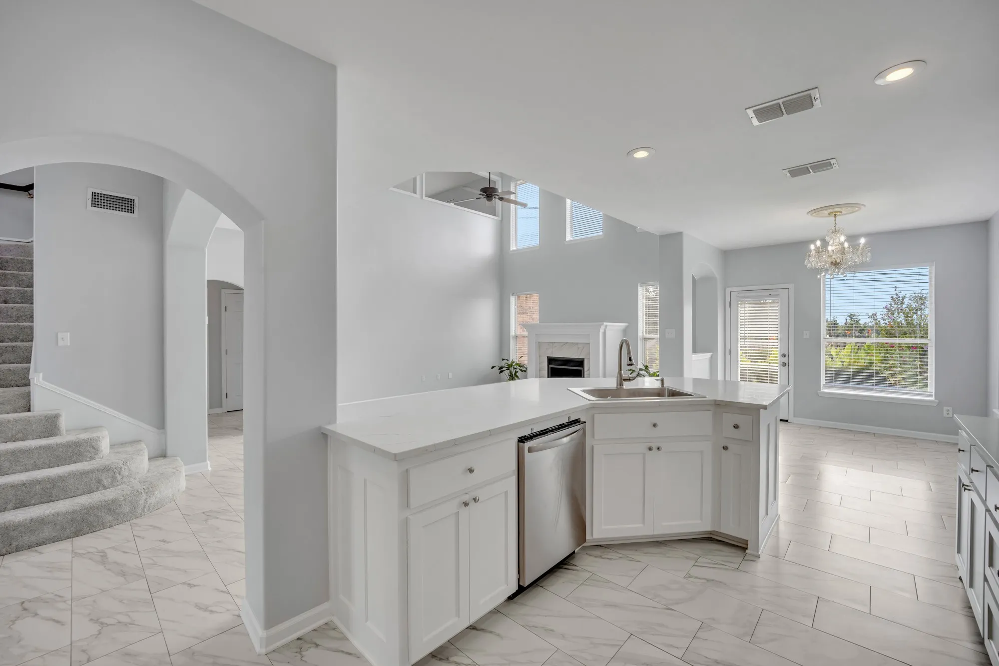 Central kitchen island with a stainless steel sink, white cabinetry, and a built-in dishwasher