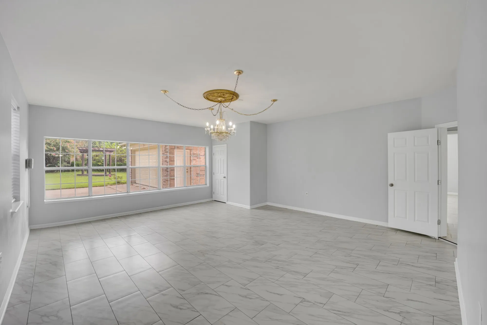 Spacious room featuring light gray walls, large rectangular floor tiles, a decorative ceiling medallion, and an ornate chandelier