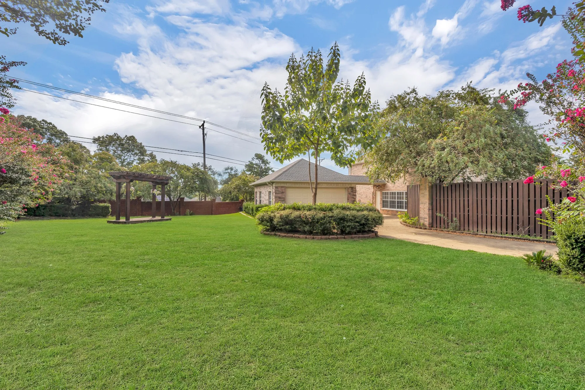 Expansive green lawn with a pergola, mature trees, and a wooden privacy fence