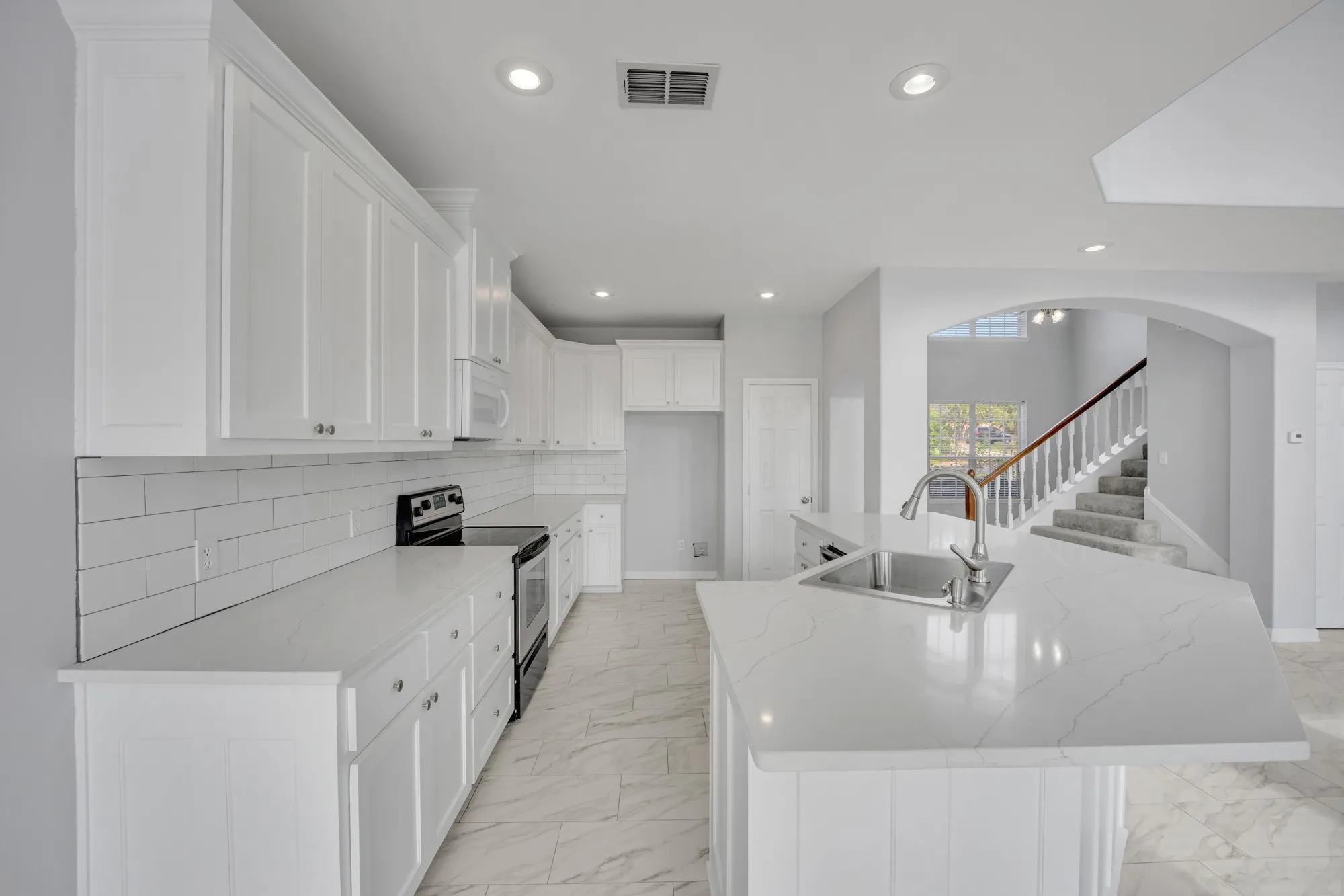 Kitchen featuring white shaker-style cabinetry, subway tile backsplash, white countertops, and a center island with an undermount sink