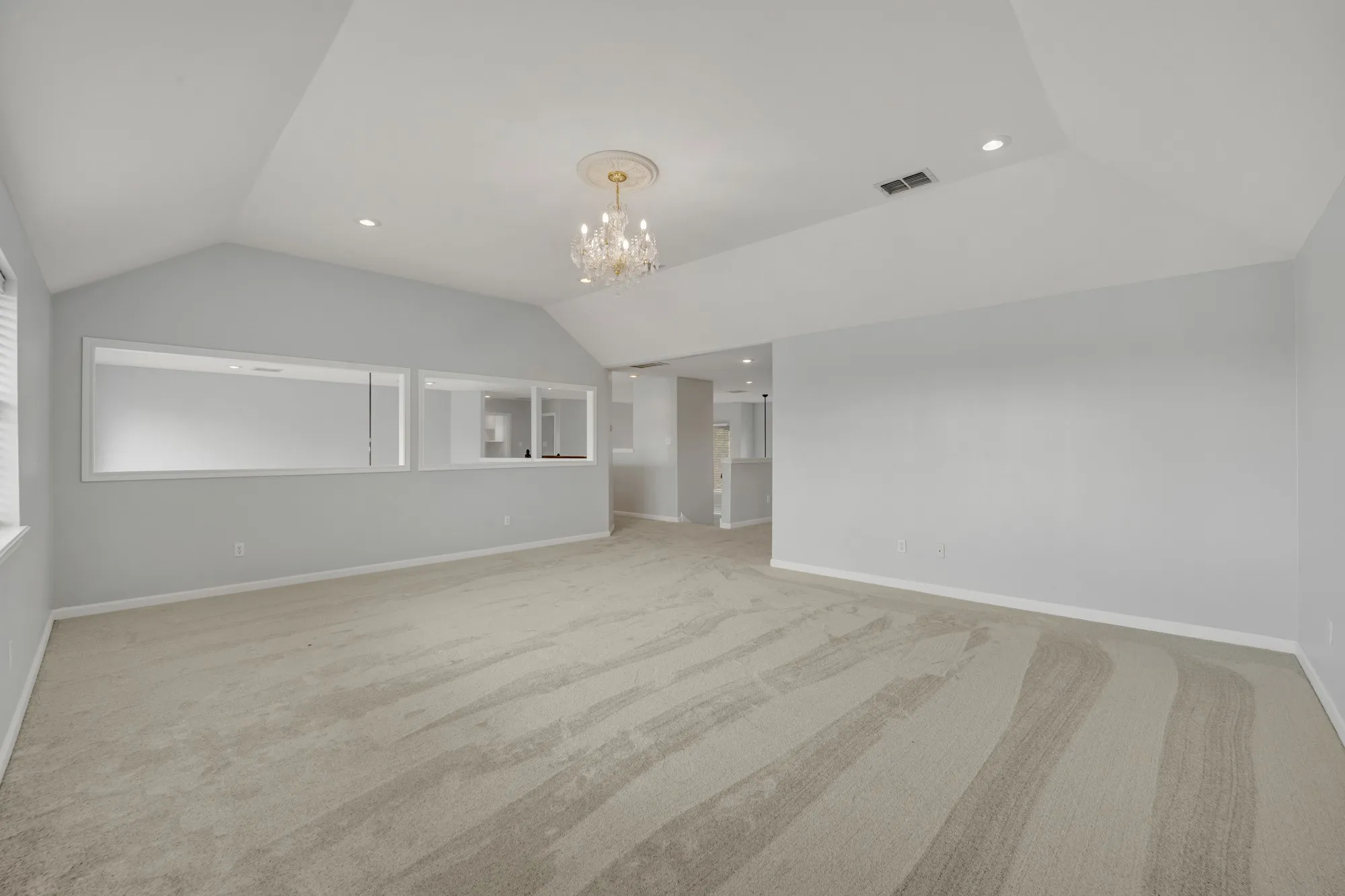 Vaulted ceiling, recessed lighting, chandelier, neutral carpeting, and interior transom windows