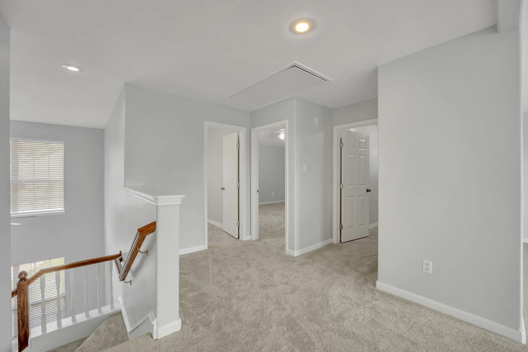 Carpeted hallway with flush-mount lighting, painted walls, and wood handrail